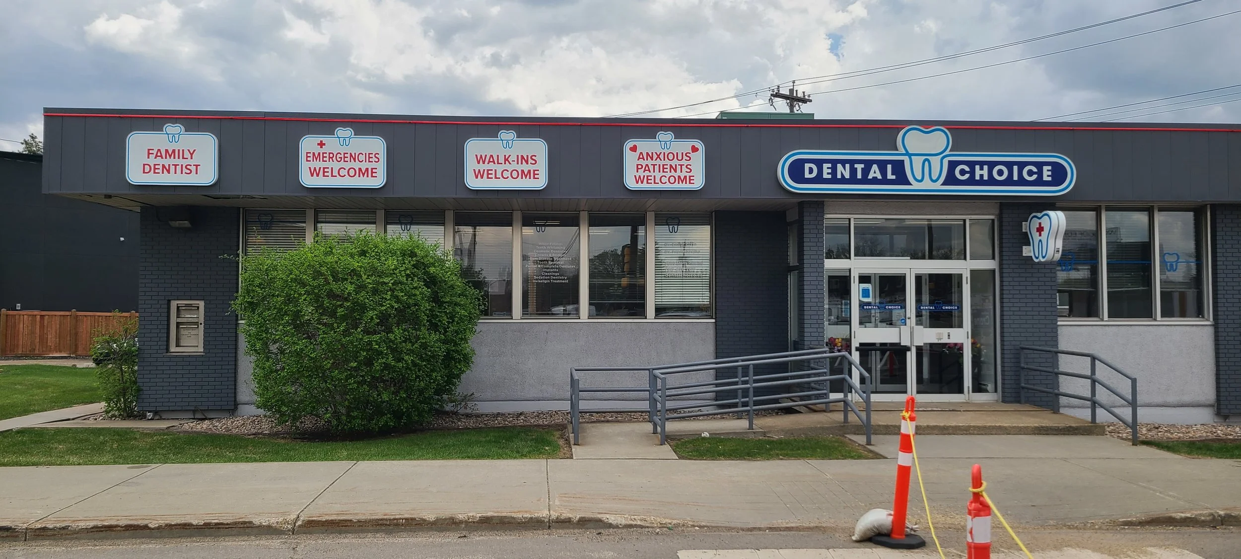 Exterior of a dental clinic with signs indicating family dentist, emergency and walk-in welcome, anxious patients welcome, and a prominent logo with a tooth.