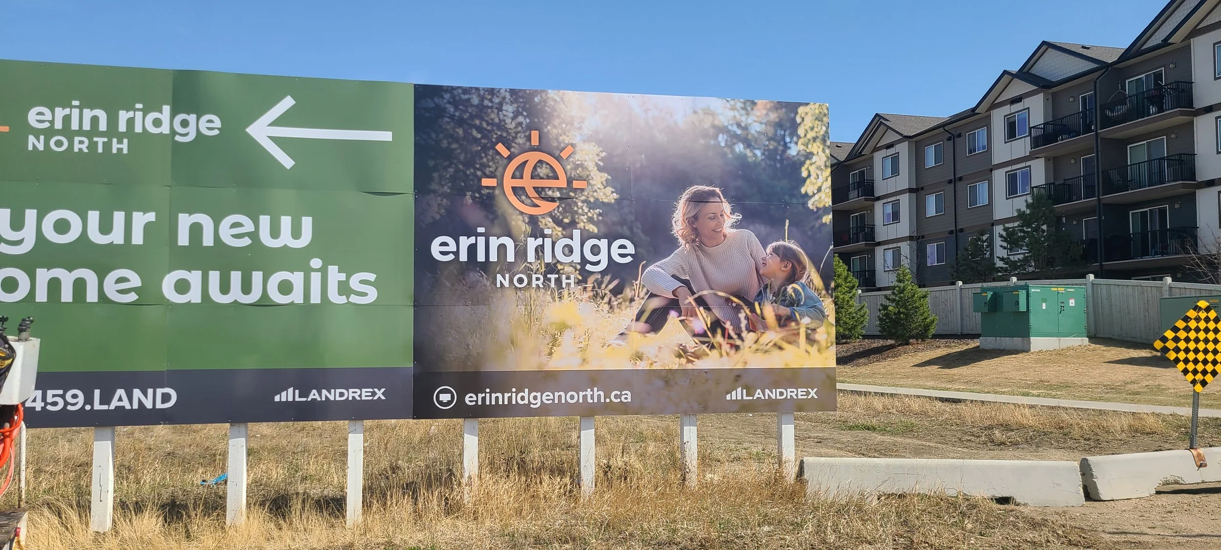 Outdoor billboard advertising Erin Ridge North residential community, featuring a woman and a girl sitting in a field of grass, with apartment buildings in the background.