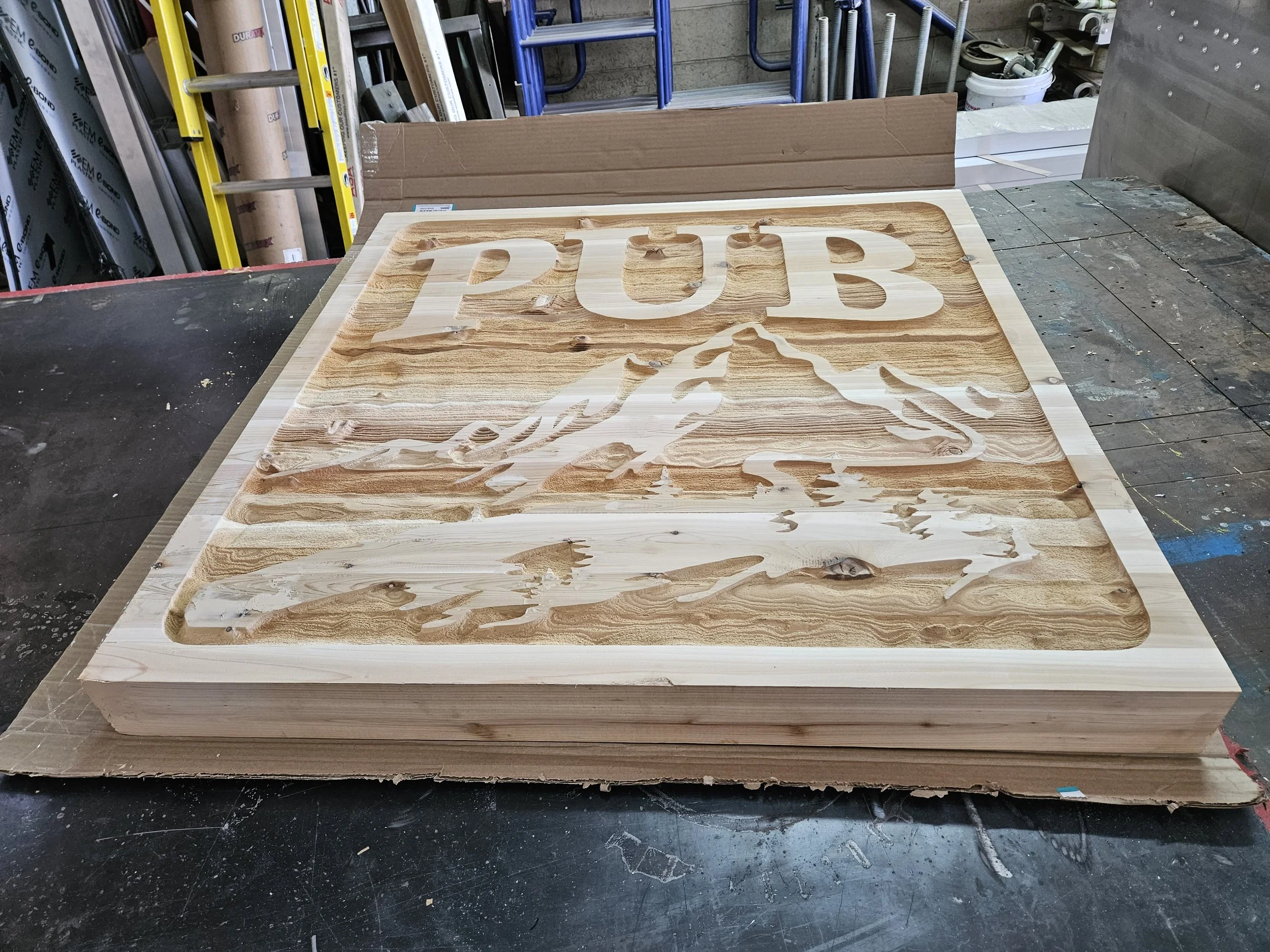 Wooden sign with the word 'PUB' cut out and a mountain design, on a workbench in a workshop.
