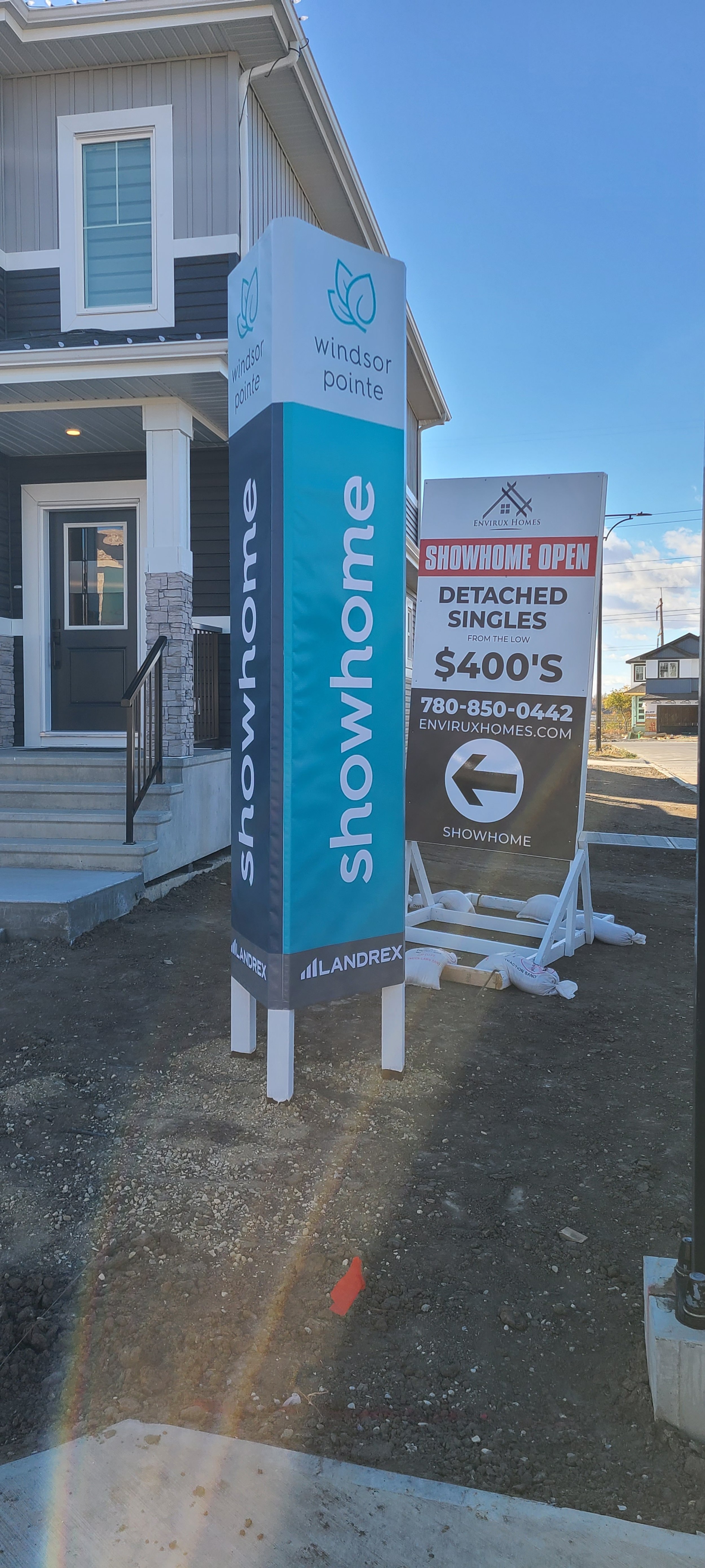 Outdoor scene with real estate signs in front of a house, advertising Windsor Pointe homes and showhome opening.