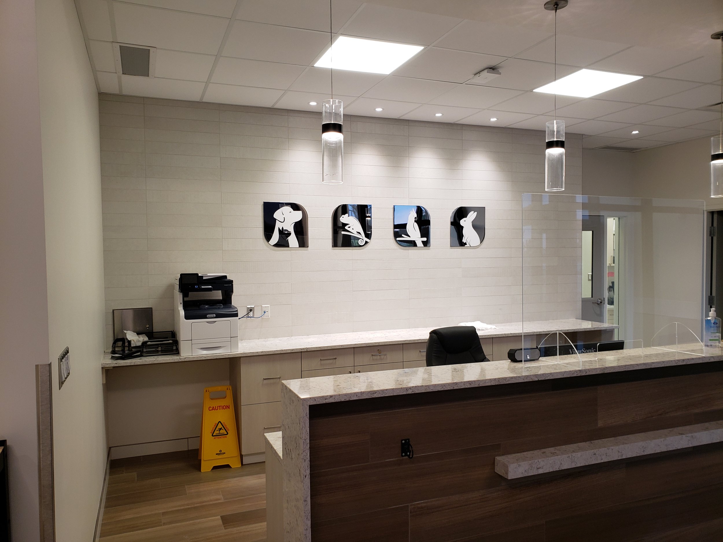 Interior of a veterinary reception area with a counter, a black office chair, wall art featuring silhouettes of dogs and cats.