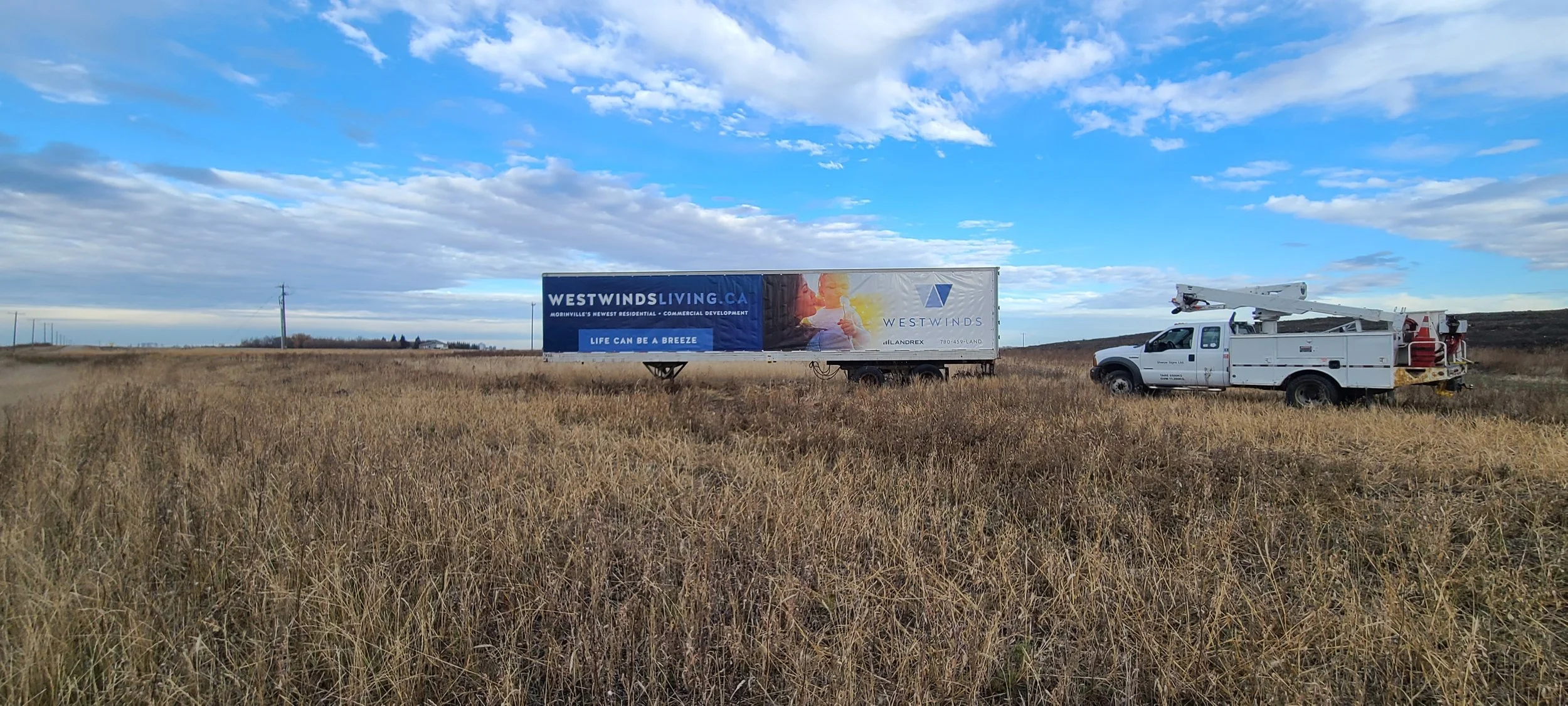 A billboard in a field advertising Westwind Living.ca, accompanied by a bucket lift.