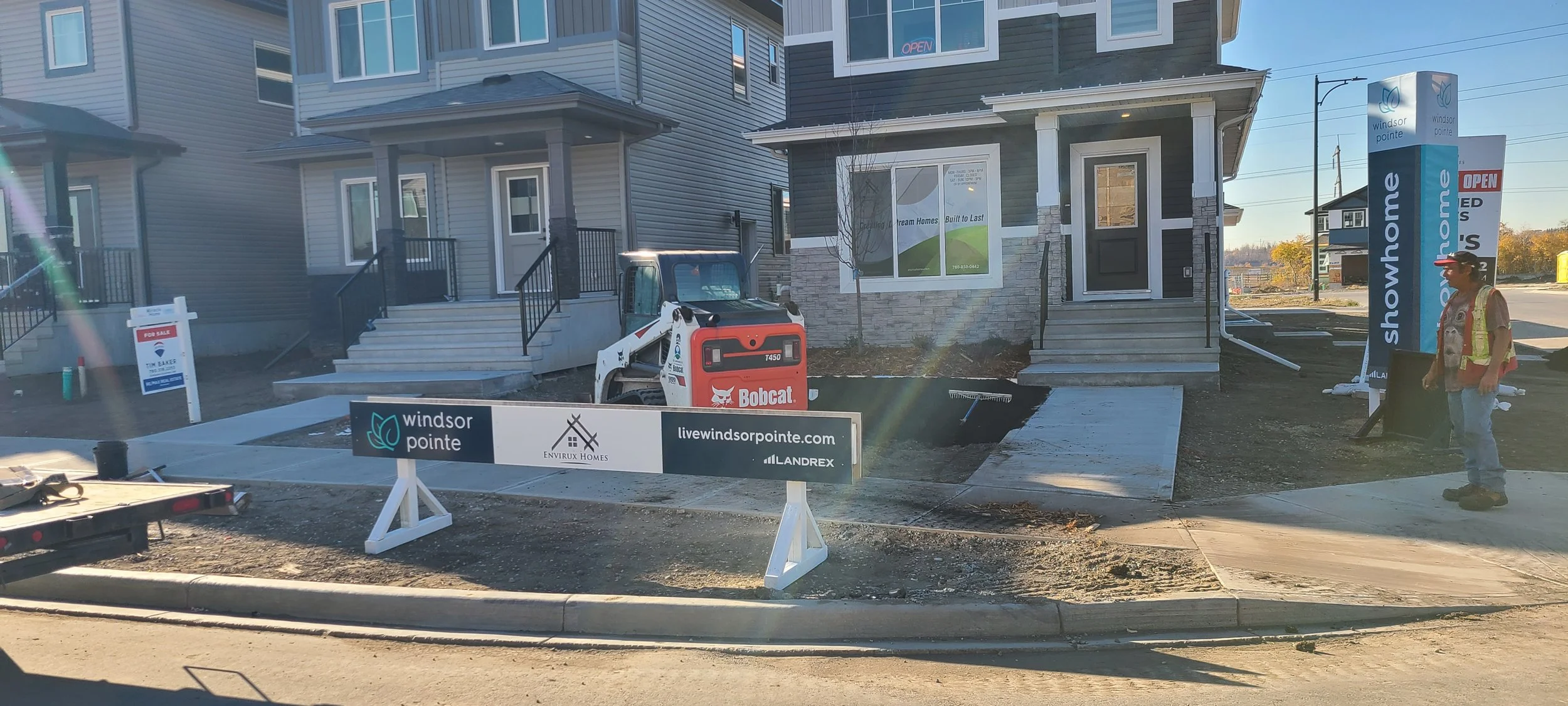 Construction site of a new townhouse, with a worker standing nearby in safety vest and cap, construction equipment, and signage for a real estate development called Windsor Pointe.