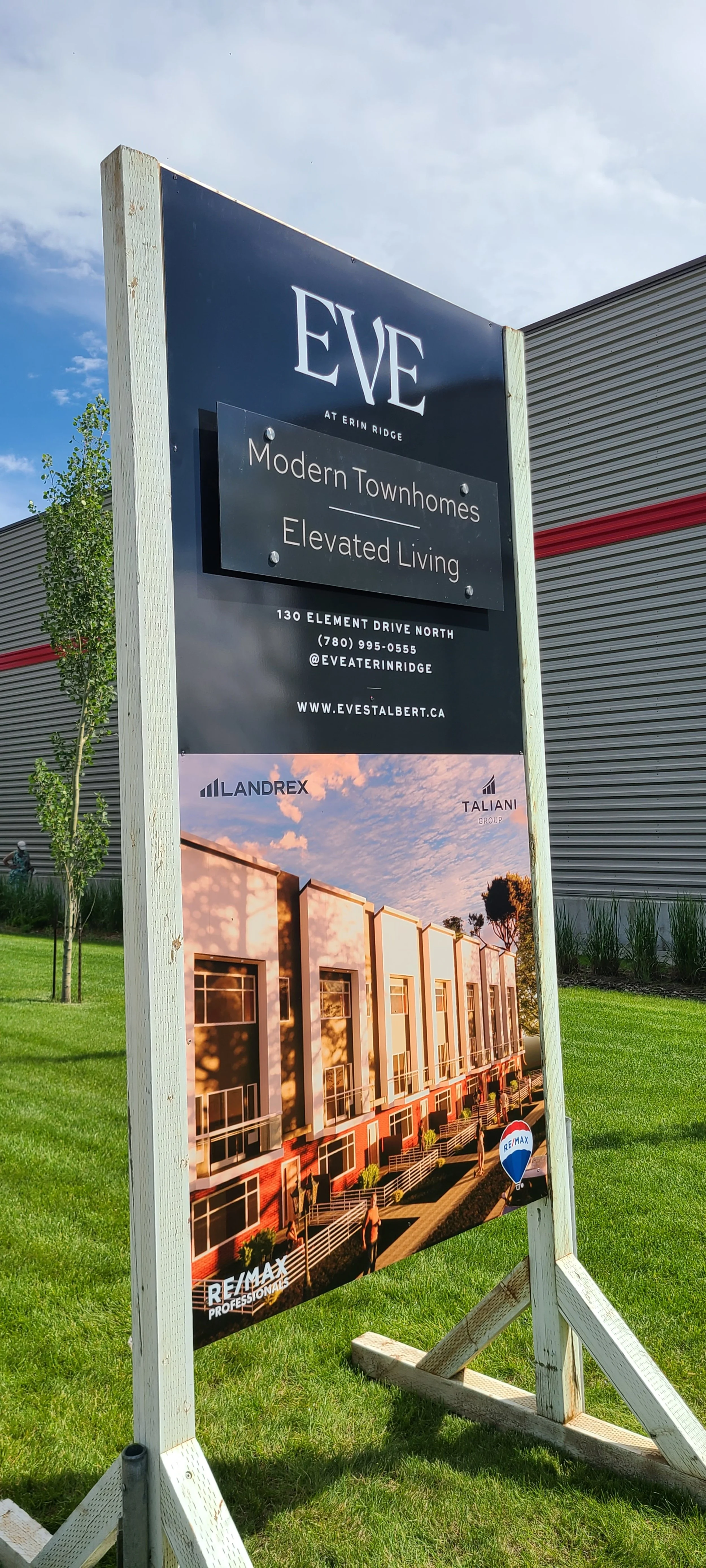 Outdoor sign advertising modern townhomes called EVE at Erin Ridge, with contact information, website, and a rendering of the townhomes exterior with a sunset sky.