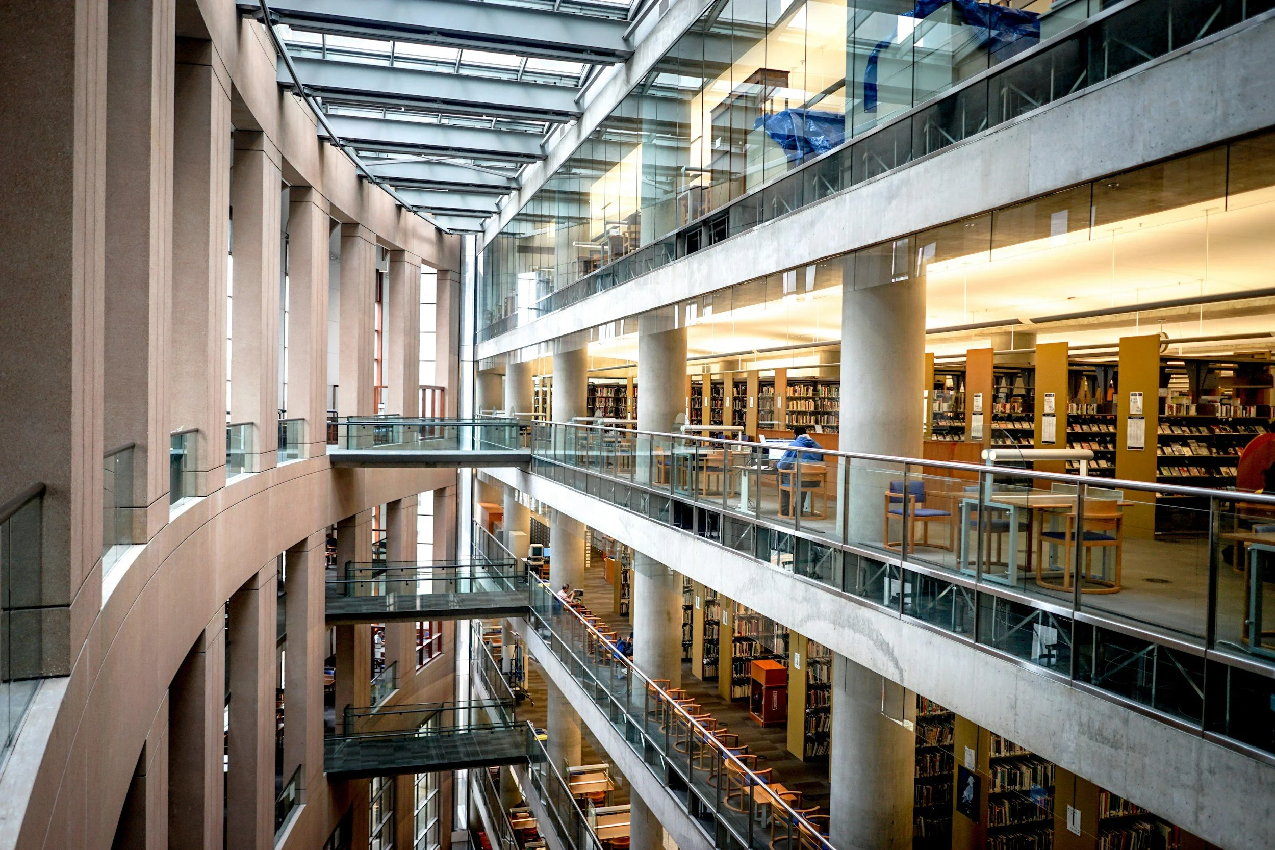 Interior of a modern, multi-level office building with open atrium, glass walls, natural light, and visible stairways connecting floors.