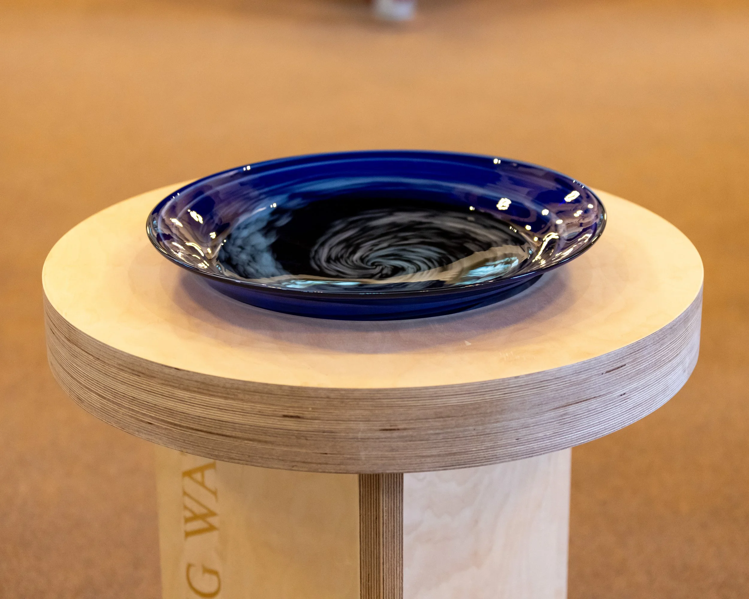 A blue glass bowl filled with swirling black and white liquid, resting on a round wooden platform.