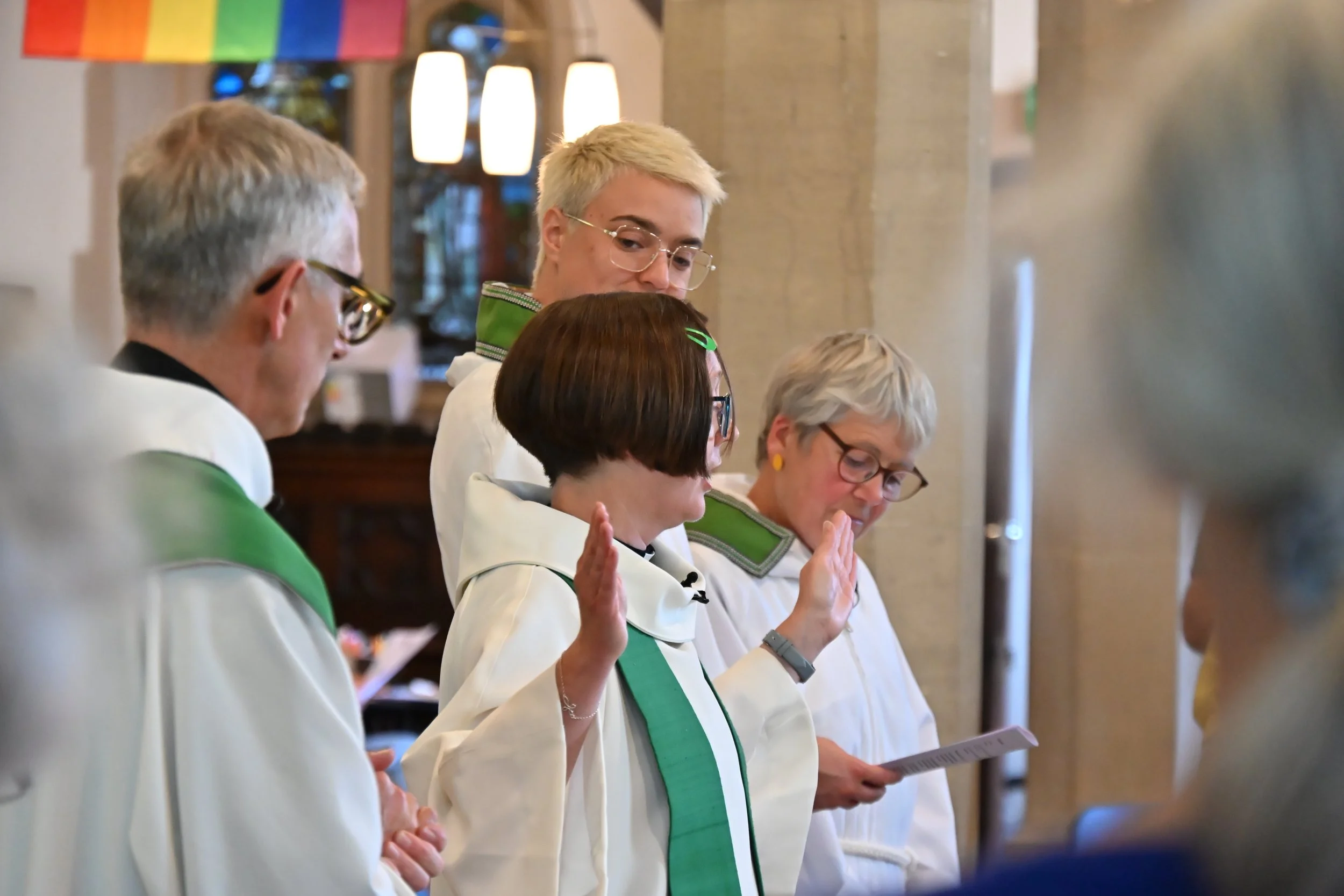 Group of people in white robes with green accents participating in a religious ceremony in a church.