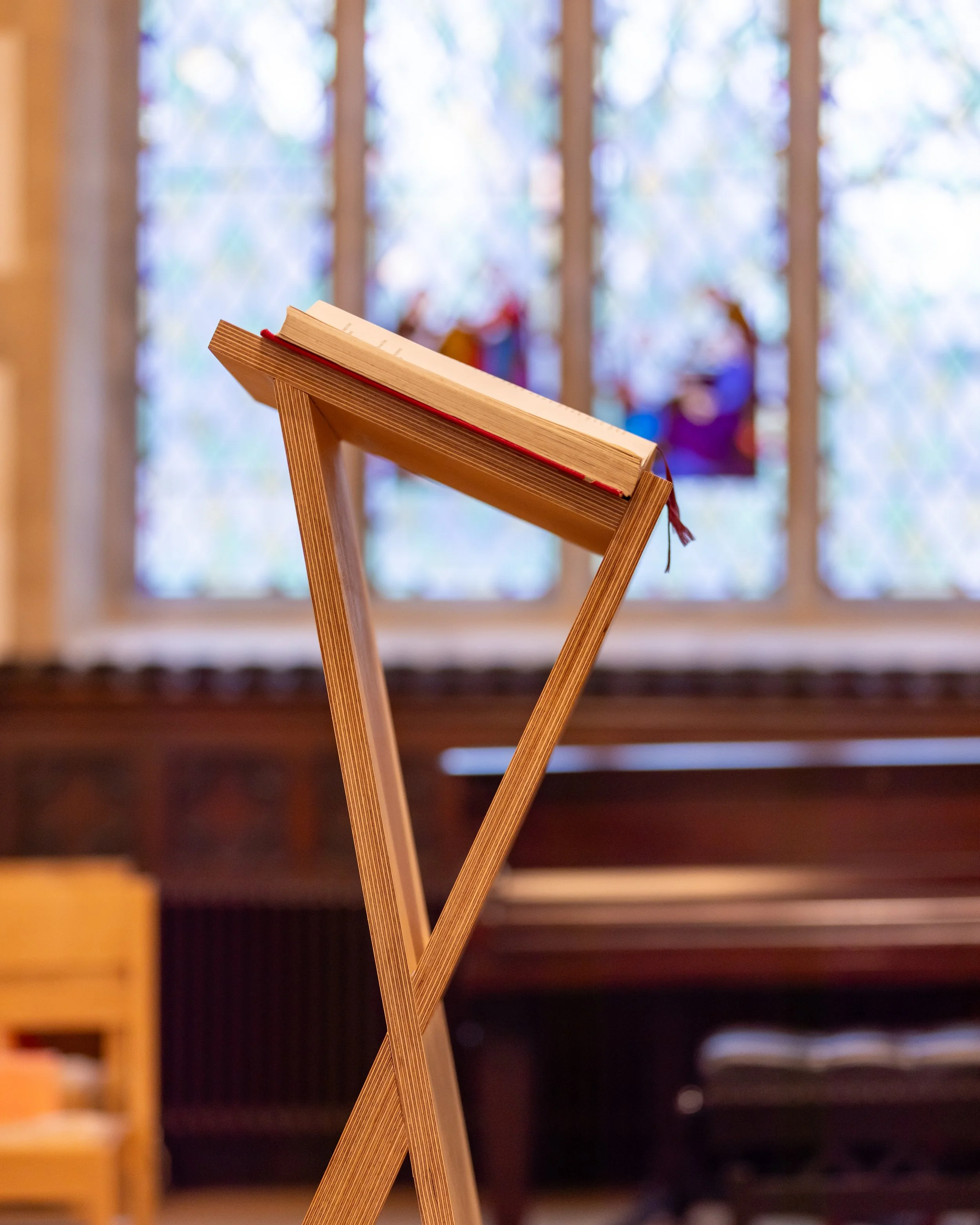 A Bible on a wooden stand inside a church with stained glass windows in the background.