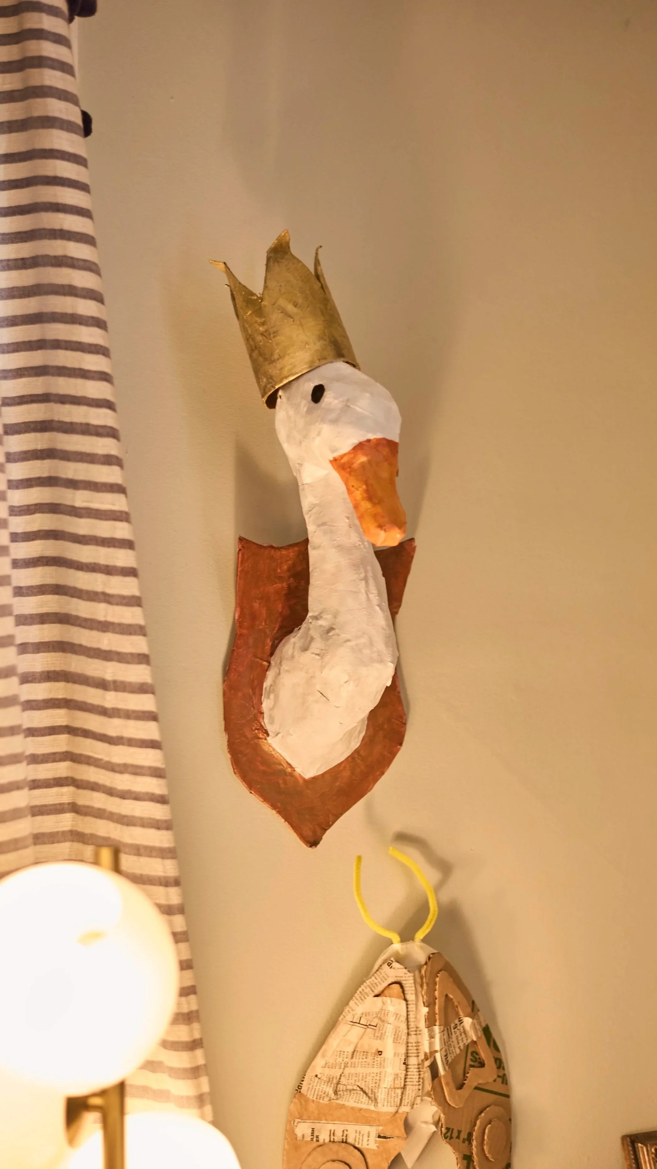A handmade paper mache sculpture of a seagull wearing a gold crown, mounted on a wall