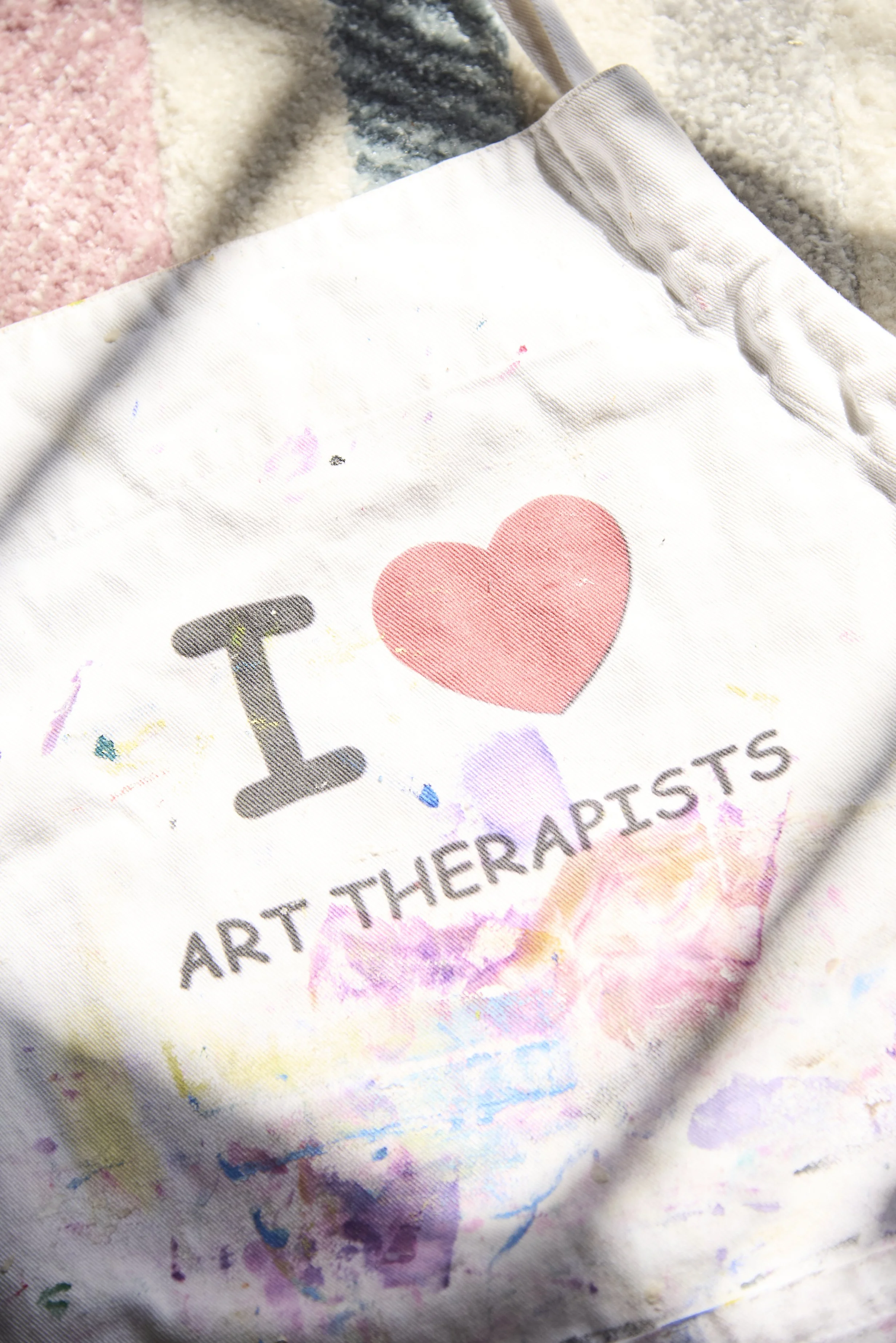 A white cloth with the text 'I ♥ ART THERAPISTS' and colorful paint splatters.