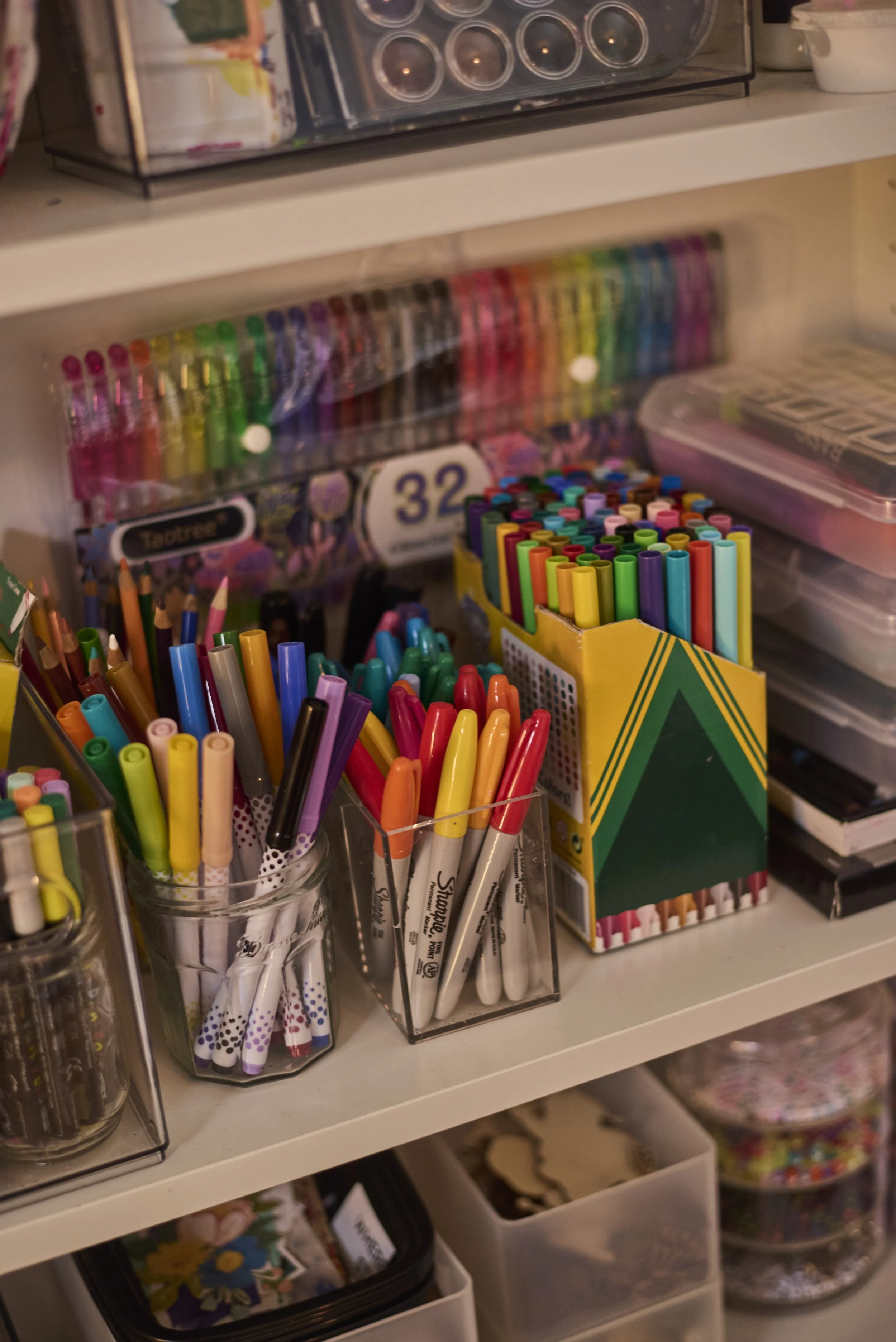 A shelf with colorful markers, pens, and art supplies organized in clear containers and boxes.