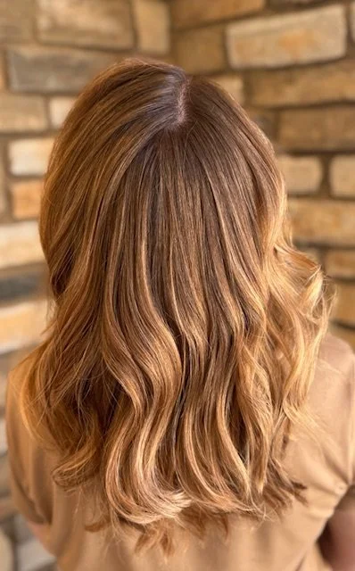 Back view of a woman's wavy, shoulder-length blonde hair against a brick wall