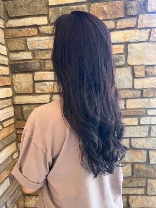 Back view of a woman with long, dark, wavy hair standing in front of a stone wall.