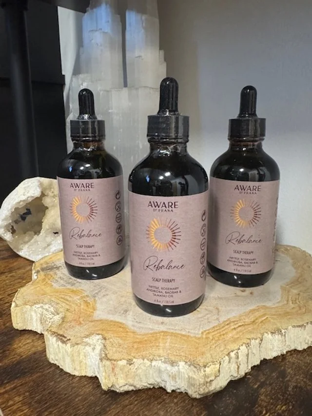 Three dark glass dropper bottles labeled 'Aware by Farina Rebalance' on a wooden surface with quartz crystals in the background.