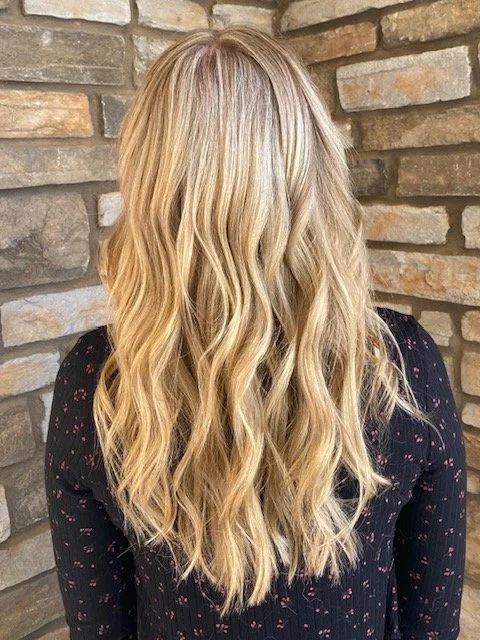 Blonde woman with wavy hair standing in front of a stone wall