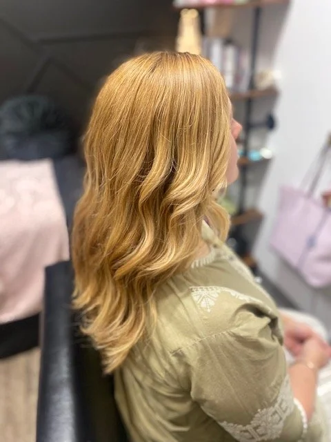 Side view of a woman with long, wavy blonde hair sitting in a salon chair.