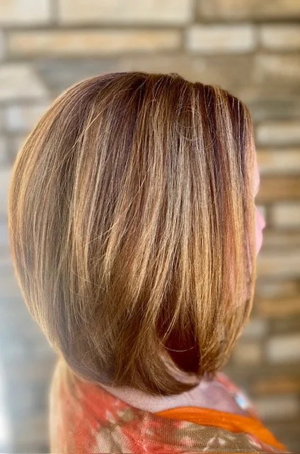 Side view of a woman's short, layered, blonde bob hairstyle with highlights, against a brick background.