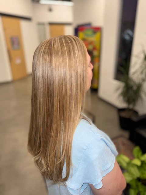 Side view of a woman with long, straight, blonde hair, wearing a light blue top, in an indoor setting.