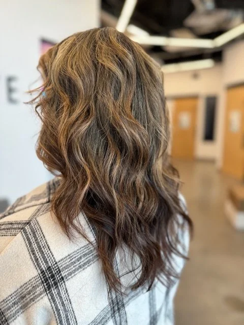 Side view of a woman with wavy, multi-colored hair in a salon.