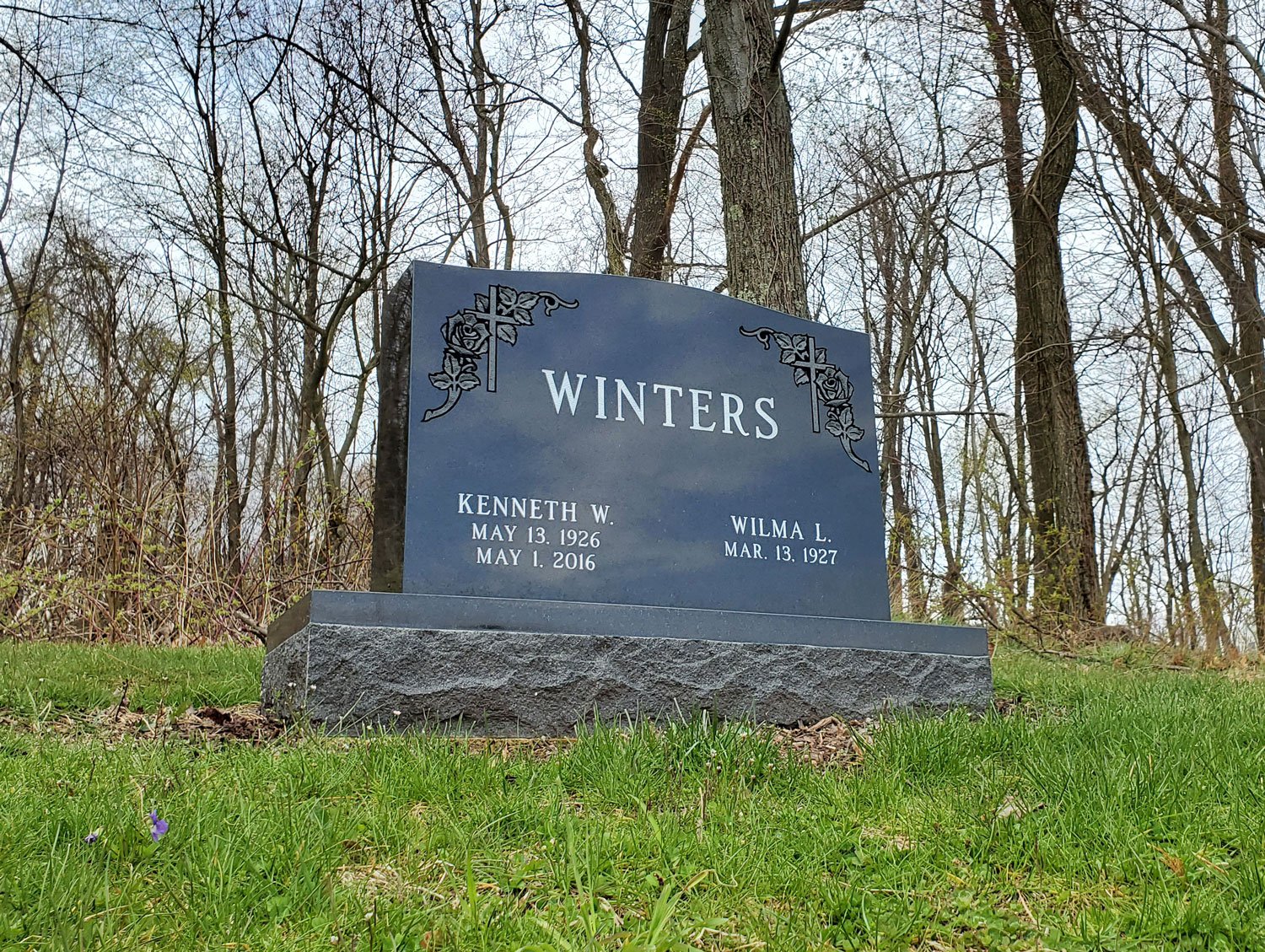 A gravestone in a wooded area with the surname Winters, commemorating Kenneth W. and Wilma L. Winters, surrounded by grass and bare trees.