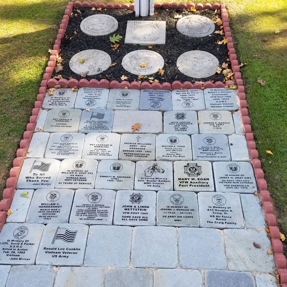 Memorial walkway with engraved bricks and plaques honoring military veterans, featuring various names, ranks, and service details.