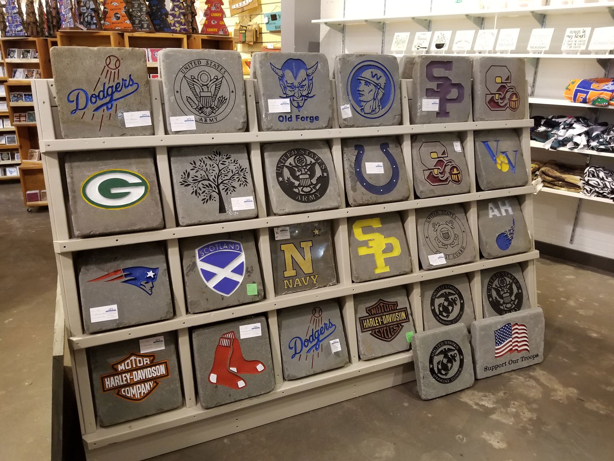 Display of engraved concrete pavers with various sports team logos and symbols, including Dodgers, Green Bay Packers, New Orleans Saints, and military insignias.