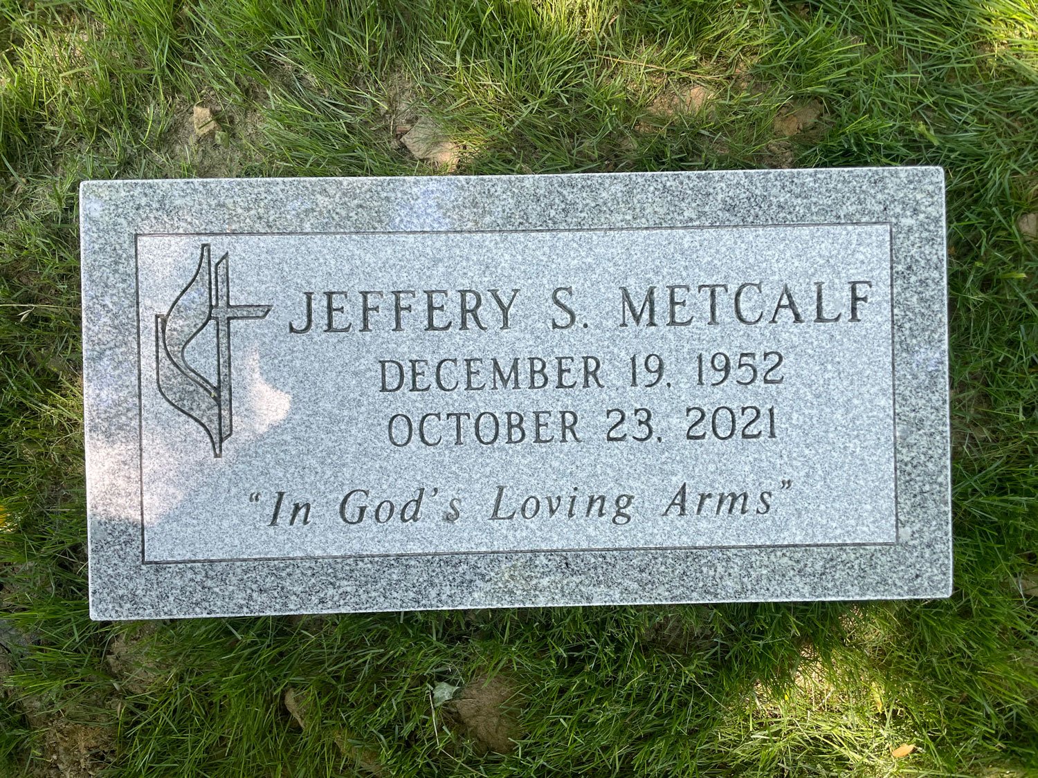 Gravestone for Jeffery S. Metcalf with the inscription: December 19, 1952, October 23, 2021, and the quote 'In God's Loving Arms'.