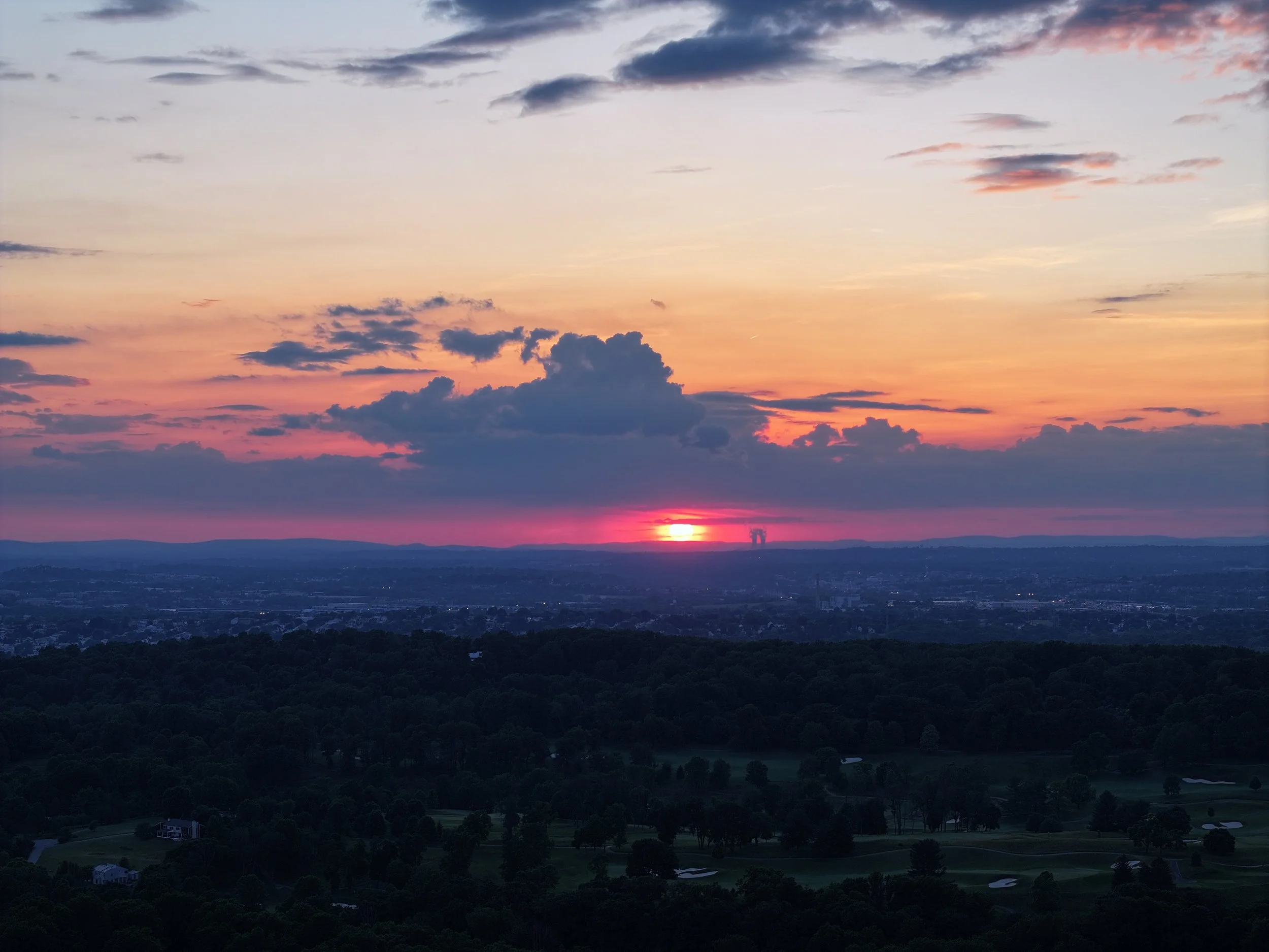 Sunset over rolling hills, with an orange and pink sky, and some clouds.