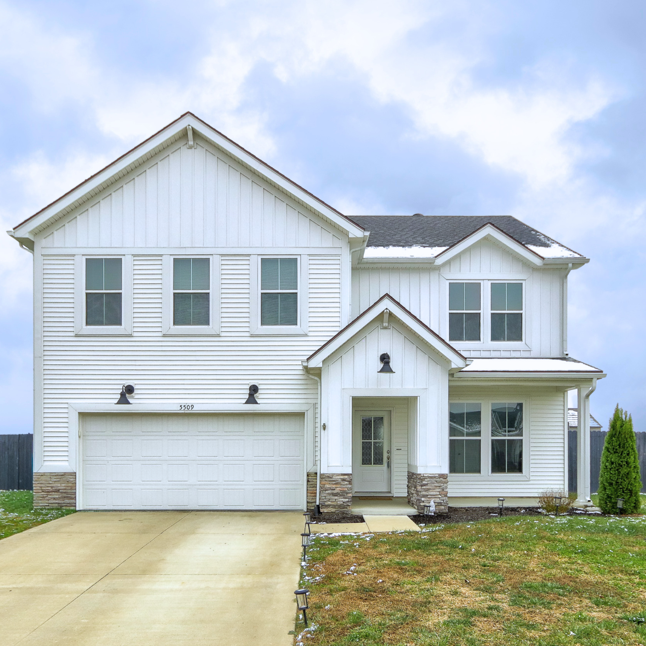 A white modern house with a garage door, multiple windows, a small front porch, adobe stone accents, and a small yard with a sidewalk and pathway, under a cloudy sky.