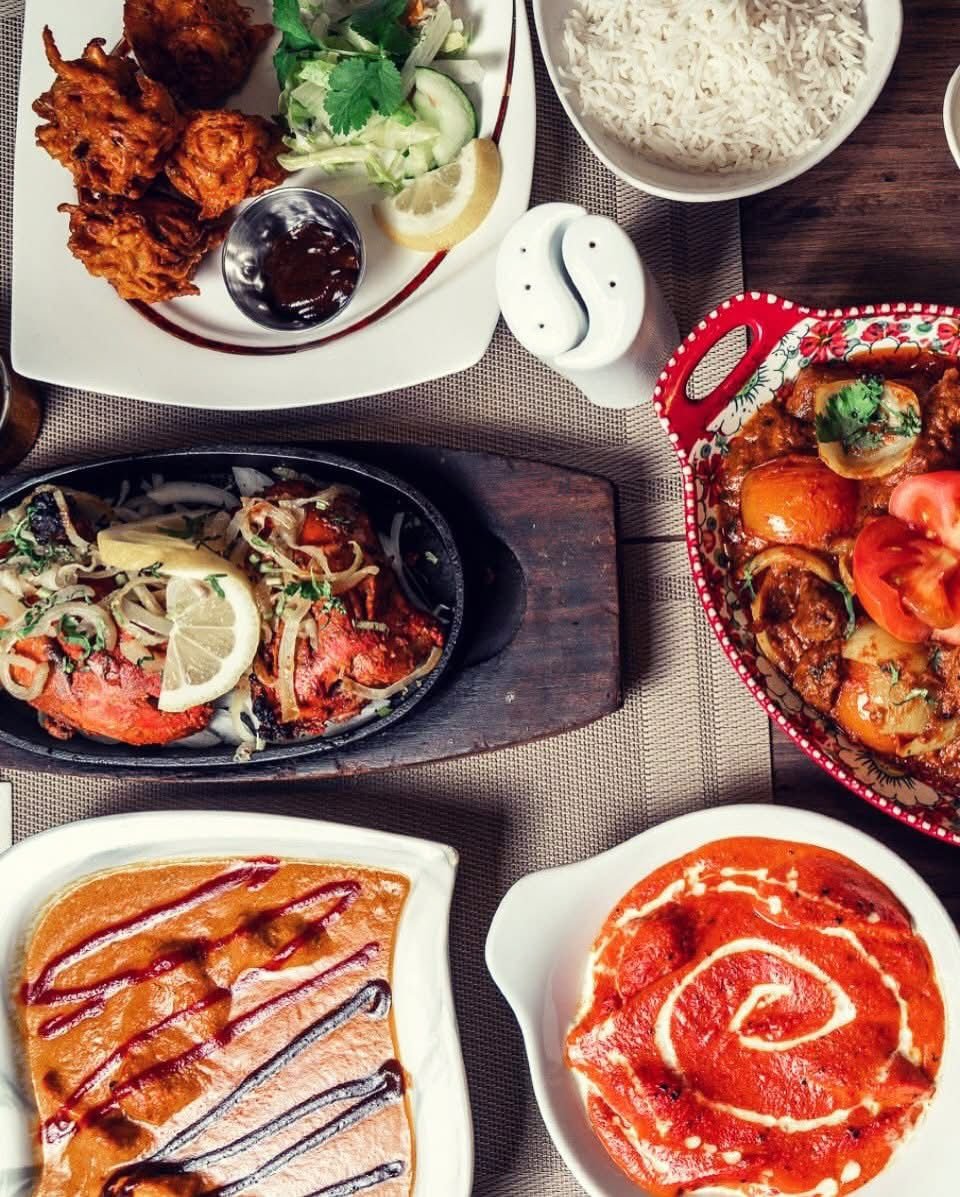 Assorted Indian cuisine dishes on a table, including fried chicken, rice, tandoori chicken, curry, and desserts with decorative bowls and lemon wedges.
