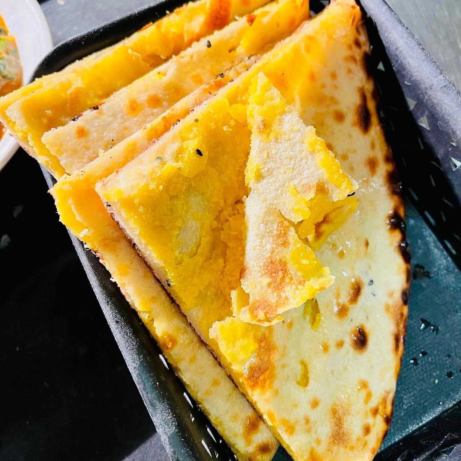 Close-up of slices of cheesy grilled flatbread in a black container.