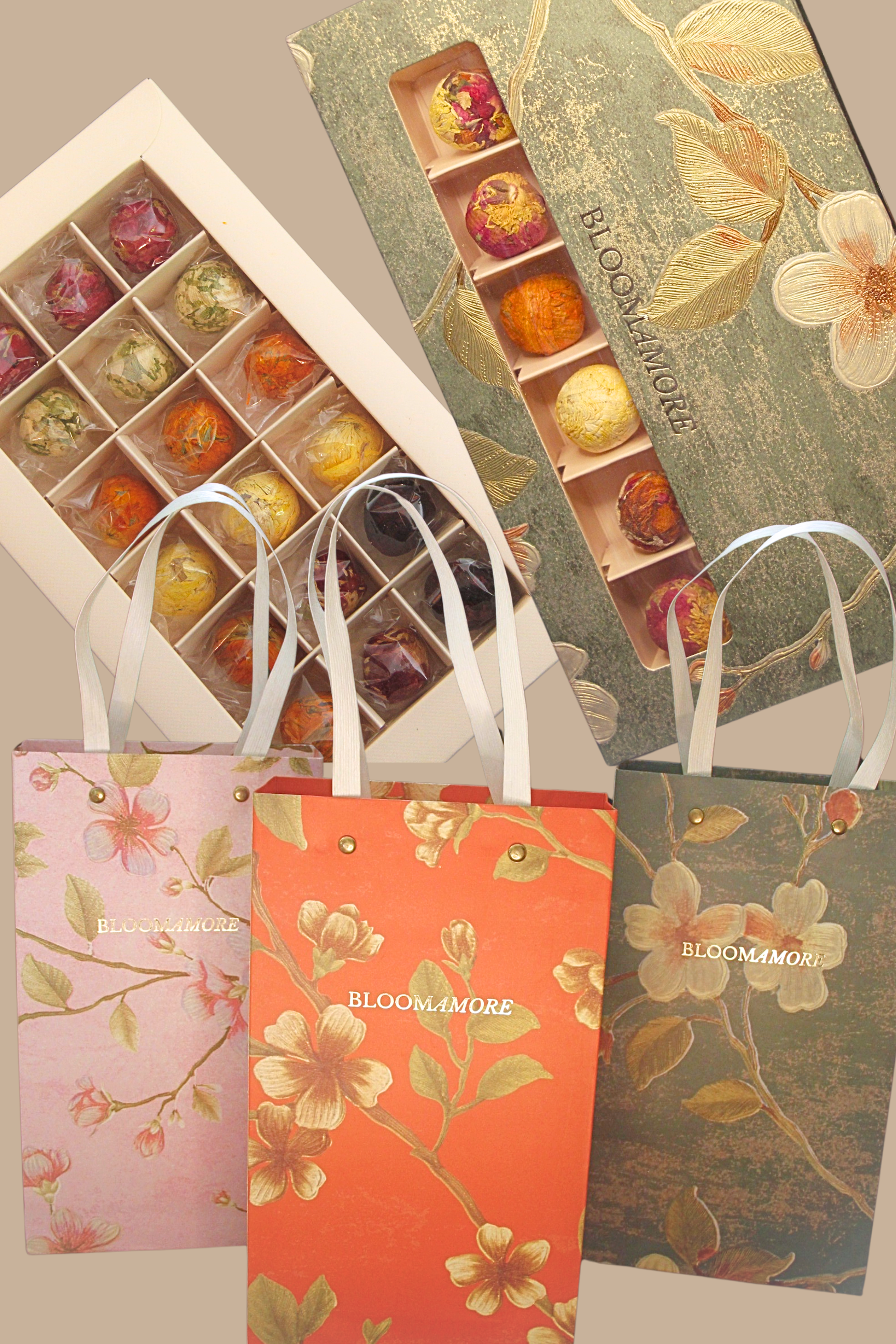Photo displays two boxes of colorful, foil-wrapped chocolates and three floral-patterned gift bags with handle straps, all with the brand name BLOOMAMORE. The boxes contain assorted chocolates with decorative wrapping.