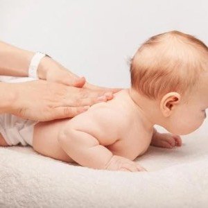 A baby lying on its stomach during a massage or chiropractic treatment, with a person's hands applying pressure on the baby's back.