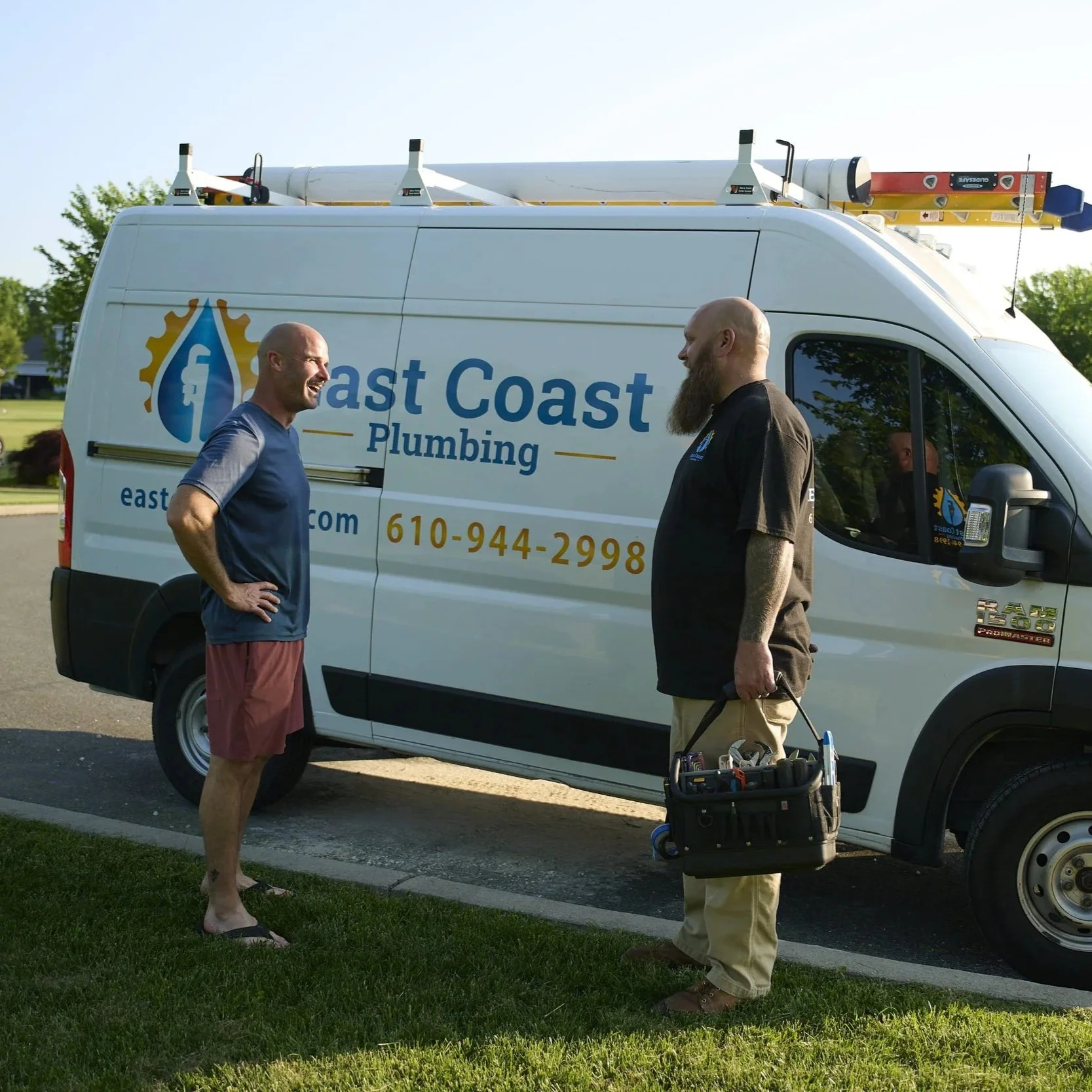 Plumbing technician discussing residential plumbing concerns with customer beside service vehicle during rental property maintenance visit.
