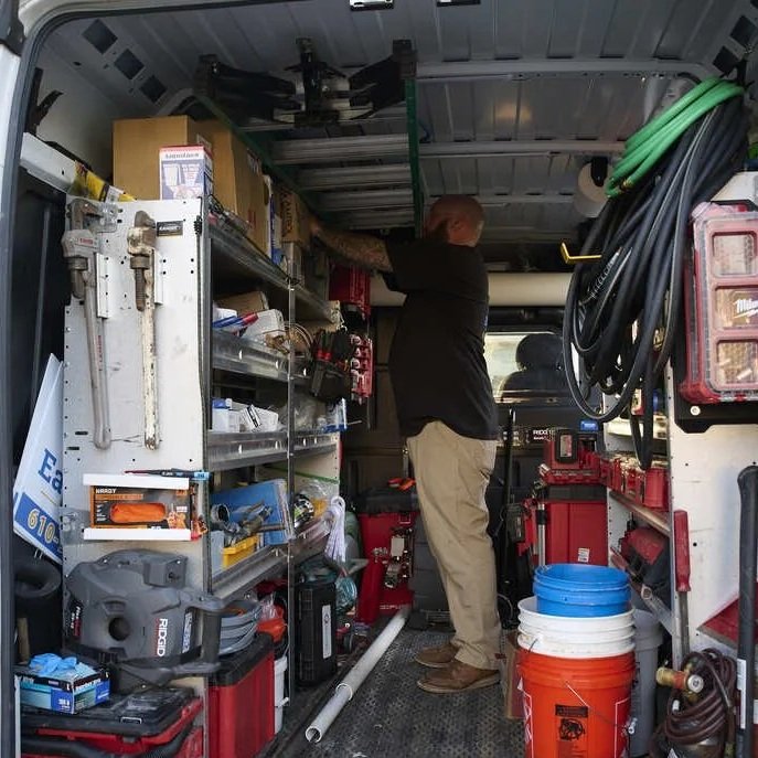Plumber inside fully stocked service van organizing drain cleaning equipment, preparing to diagnose and prevent commercial drain backups.