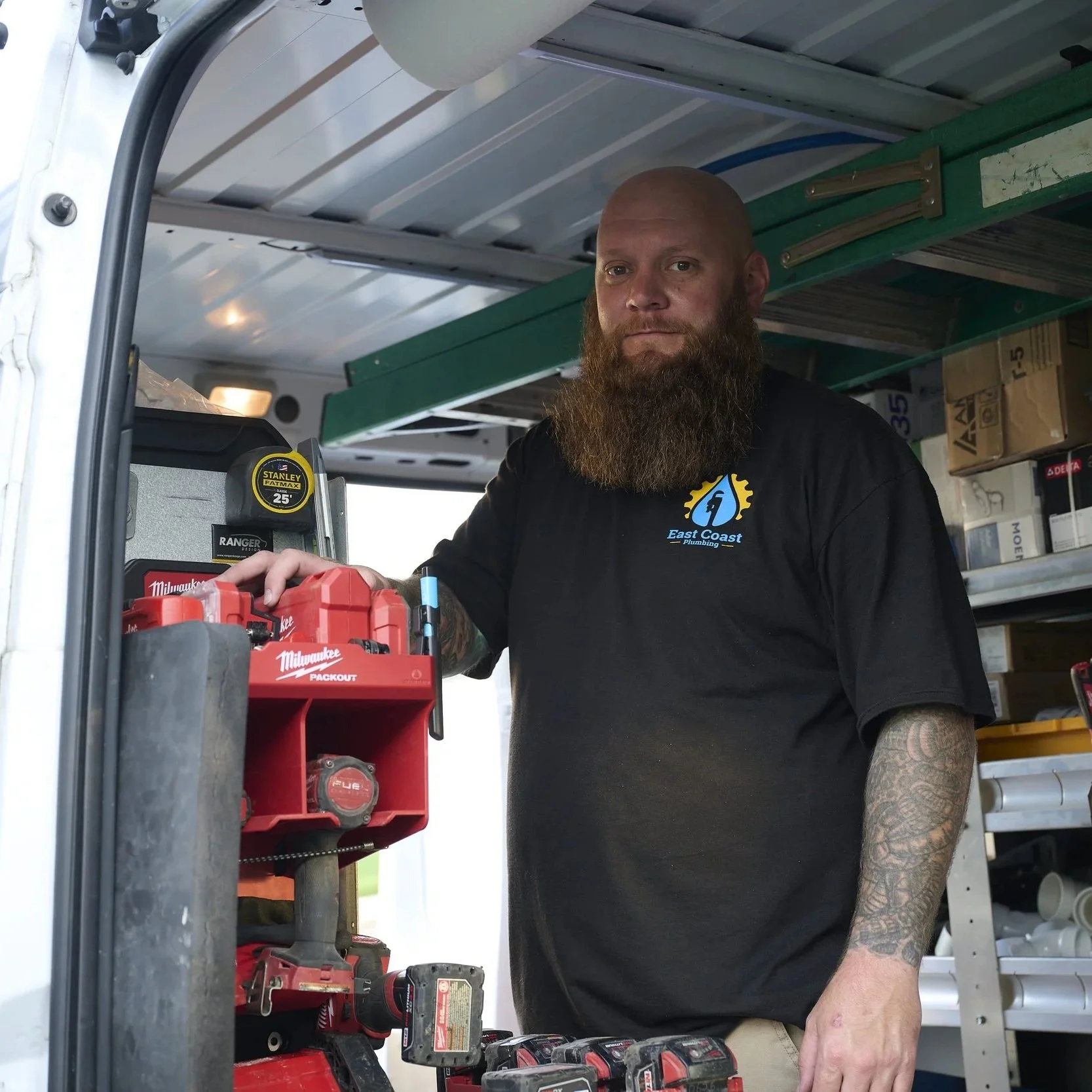 Plumber standing inside service van stocked with tools and equipment, preparing for drain cleaning and plumbing repair.