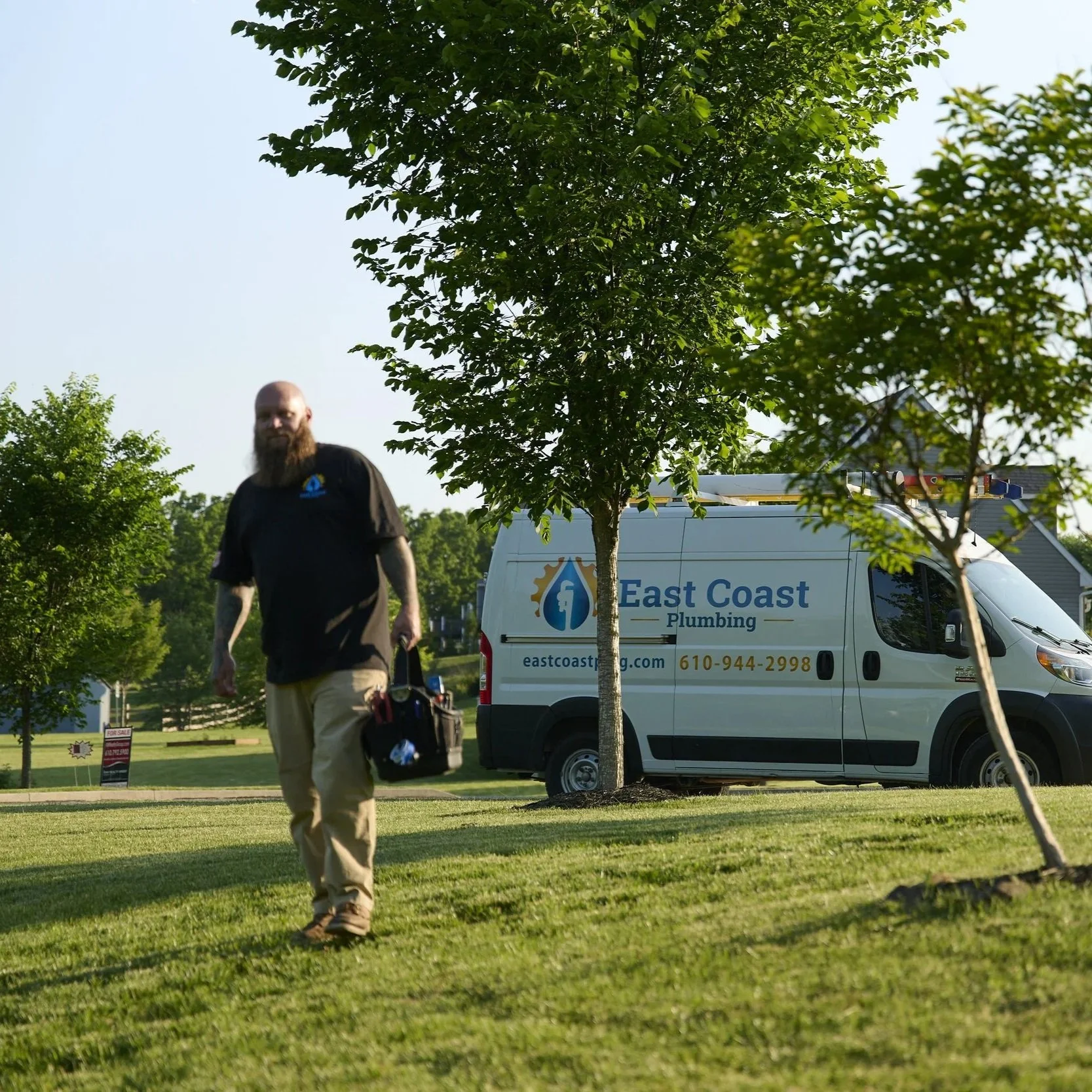 Plumber walking across residential lawn near service van, preparing for sewer line inspection, repair, or replacement service call.