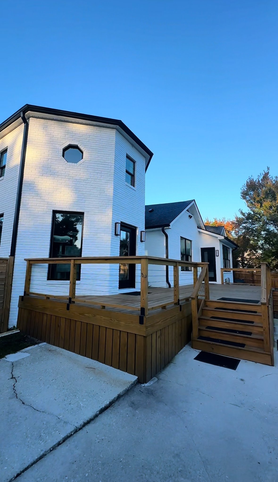 New white house with a wooden deck and stairs, black window frames, and a clear blue sky.