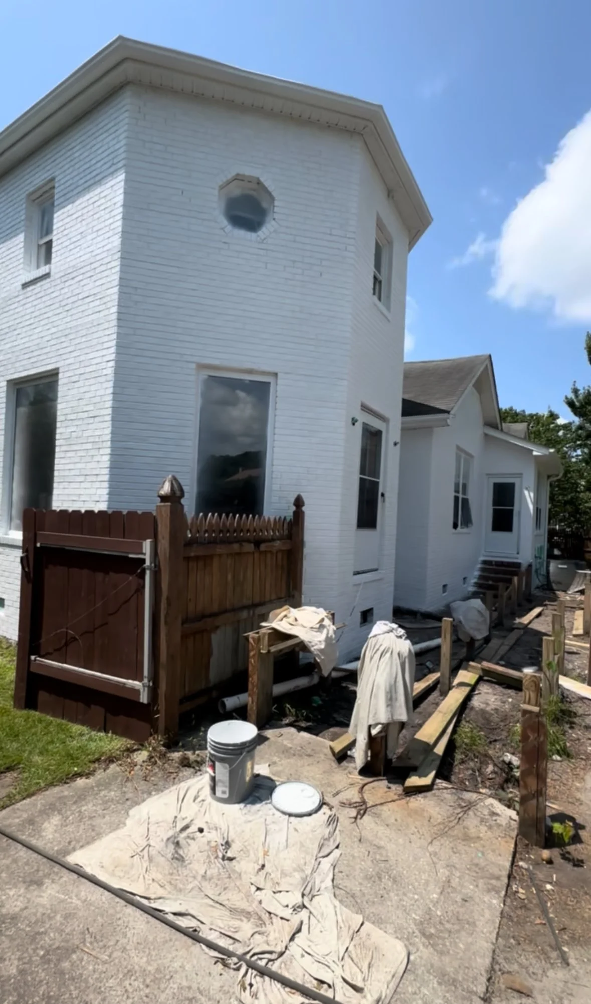 House under renovation with wooden fence, construction materials, and tools outside on a sunny day.