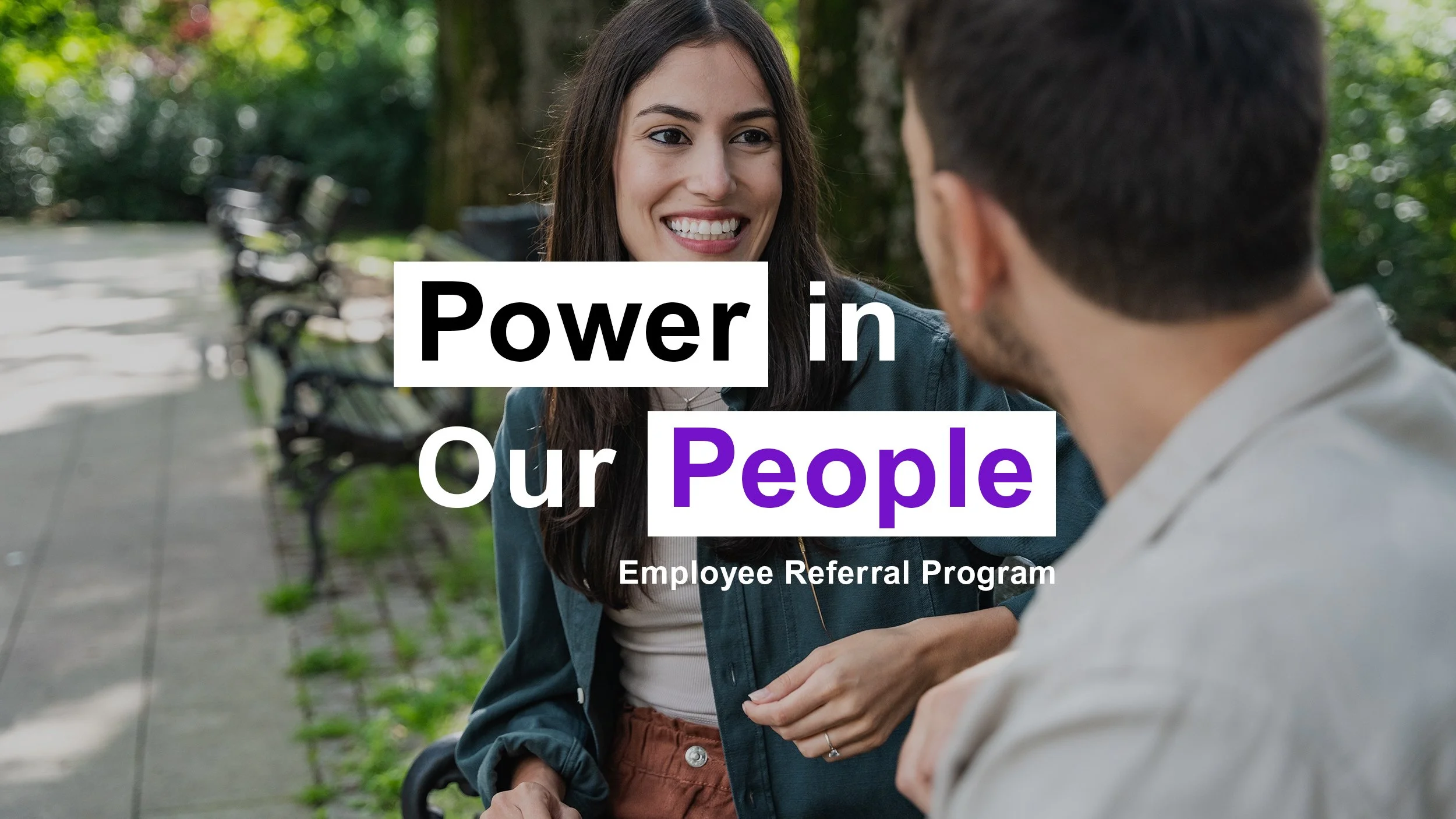 A woman smiling and talking to a man sitting outdoors in a park with benches and trees.