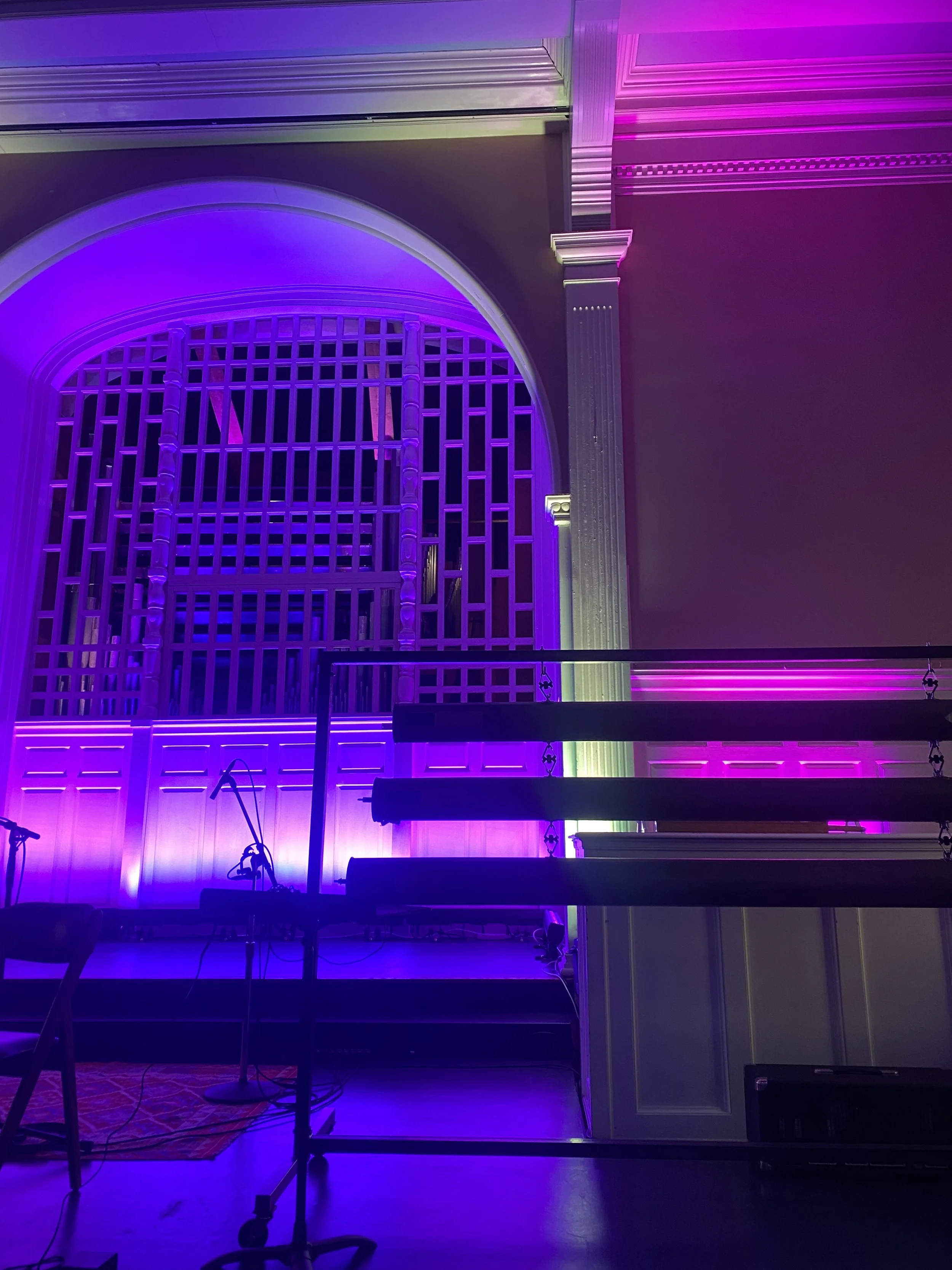 Stage with purple and green lighting, microphone stands, and a large decorative wall with an arch and lattice design.