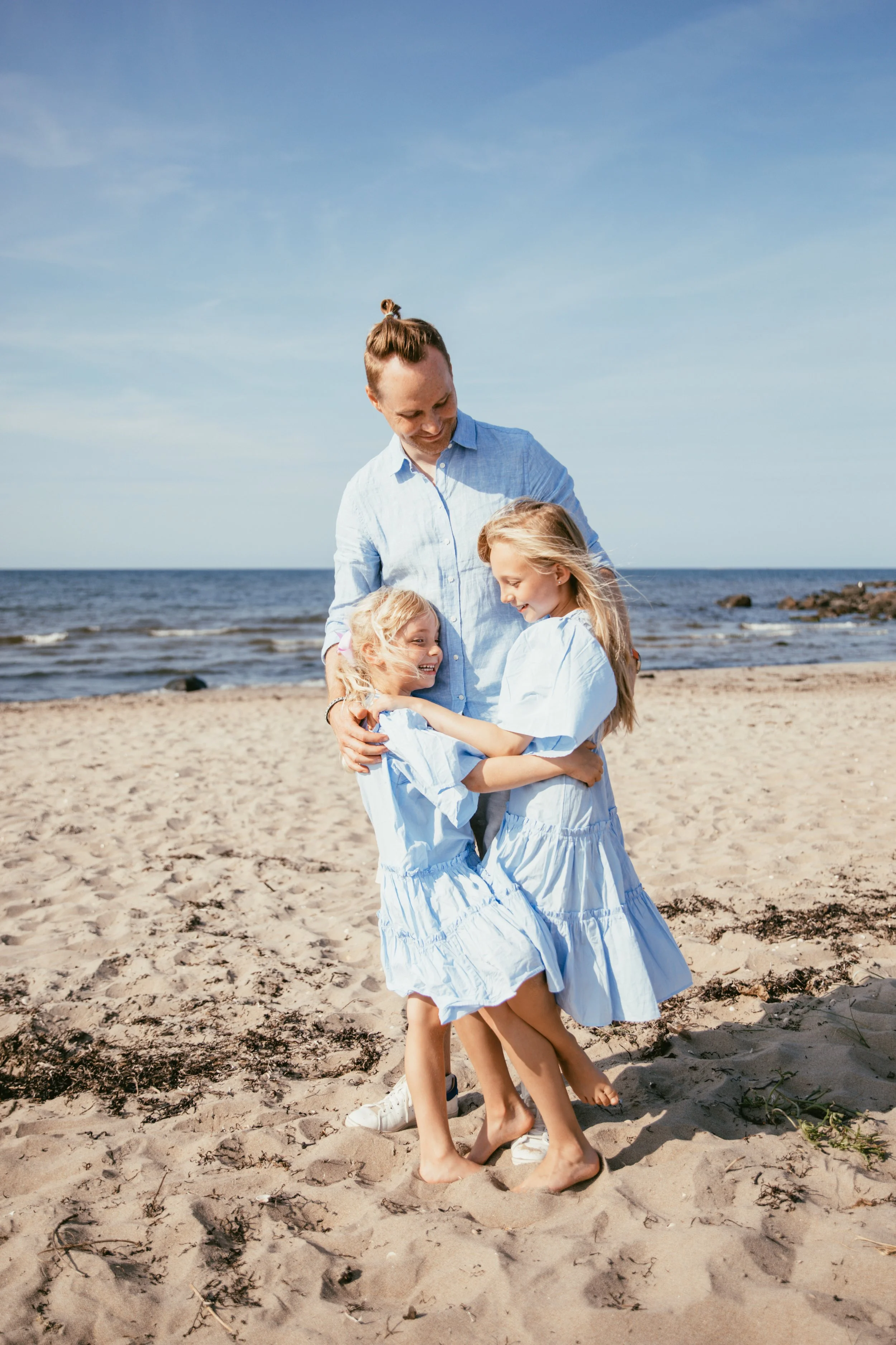 Familj står på en sandstrand vid havet, alla klädda i blått.