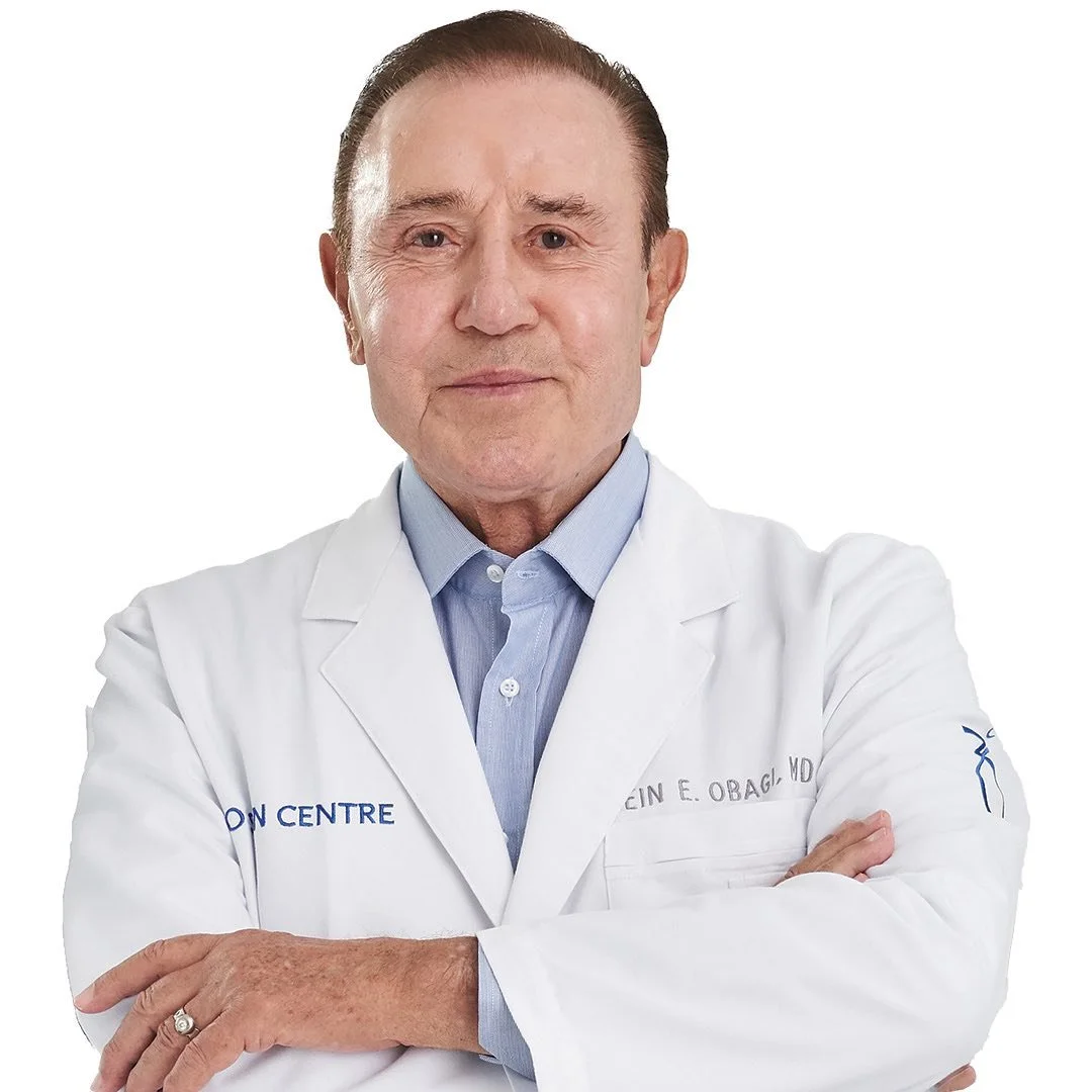 En ældre mand i hvidt medicinsk kit med arme krydsede står mod en hvid baggrund.