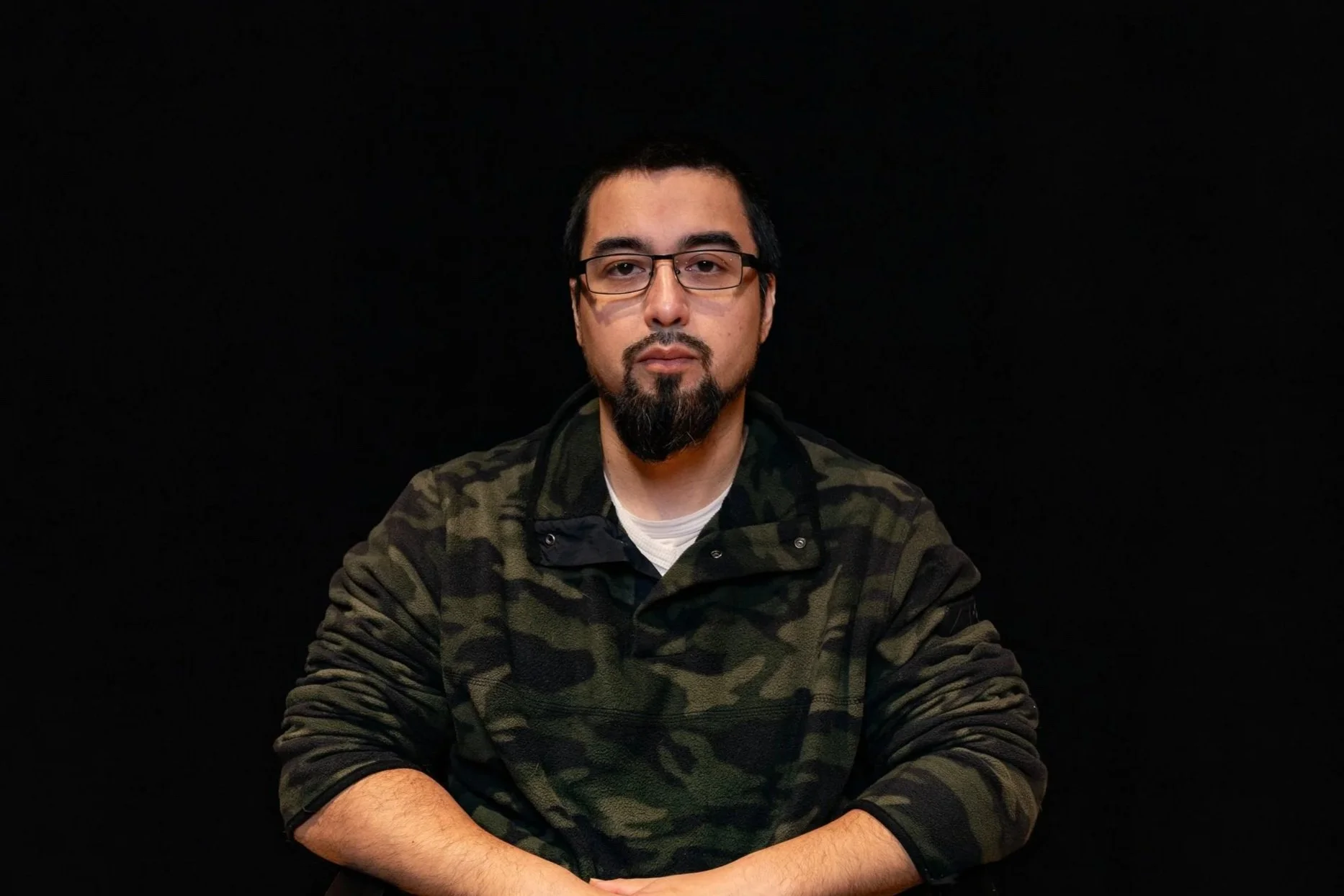 A young man wearing a black beanie and black shirt with a gold chain, taking a selfie in a bathroom.