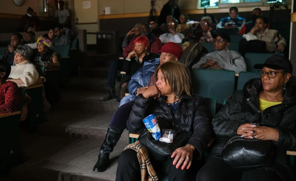 Audience members seated in a theater or auditorium, attentively watching a presentation or performance.