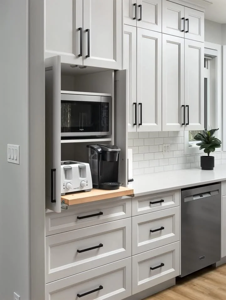 Kitchen with white cabinets, a microwave, a coffee maker, two toasters, a dishwasher, and a small plant on the countertop.