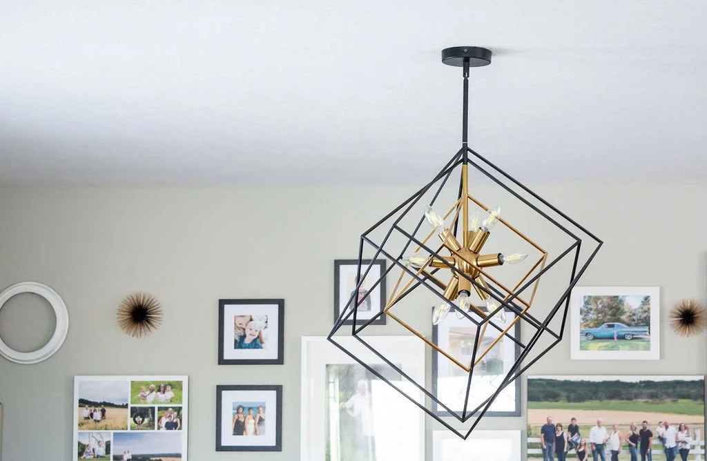 Modern geometric chandelier hanging from ceiling in a room with photo wall and wall decor