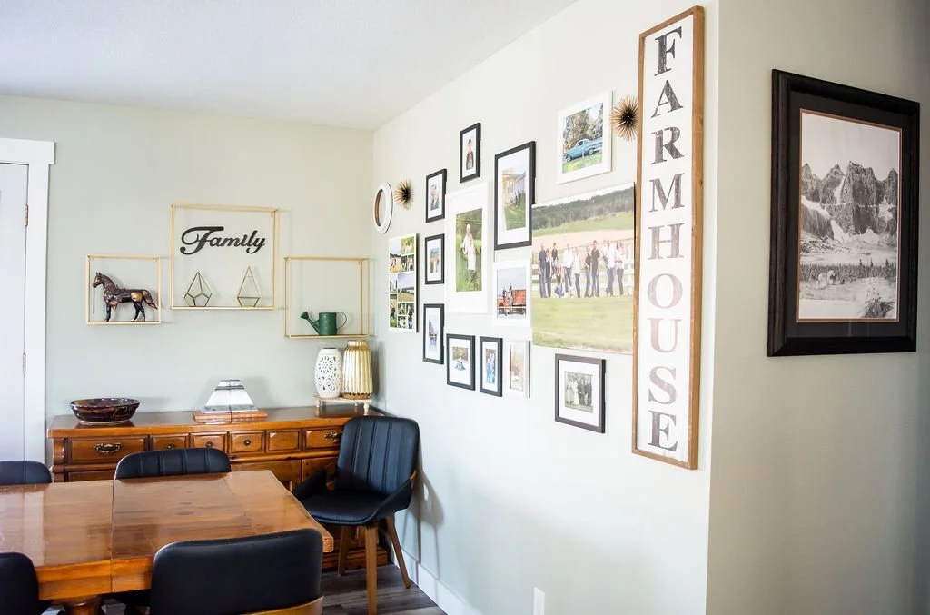 Dining room with a wooden table, black chairs, and a wall decorated with family photos, wall art, and a large sign reading 'FARMHOUSE'.