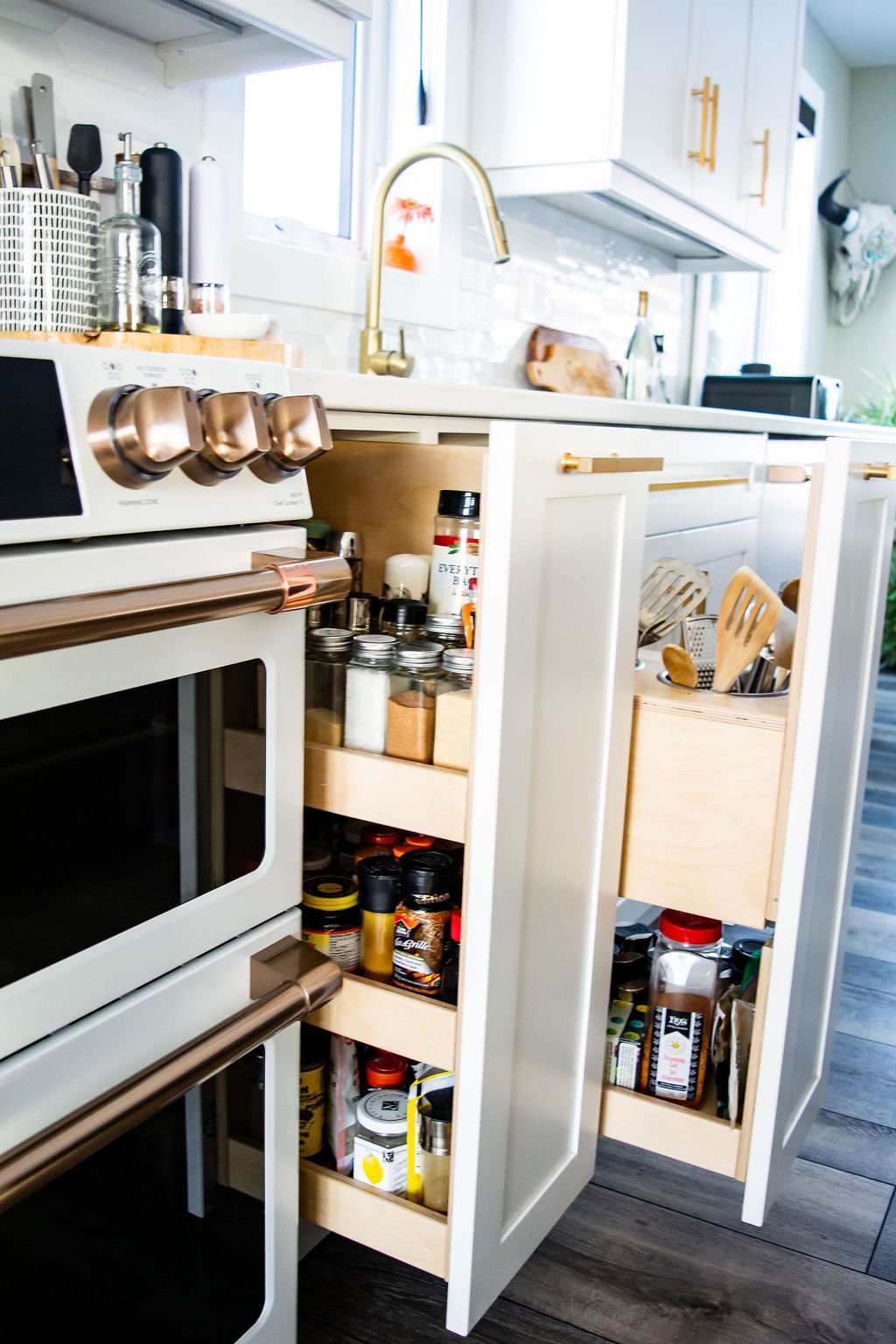 Open kitchen cabinet with spices, oils, and cooking supplies inside, stove and countertop visible in the background.