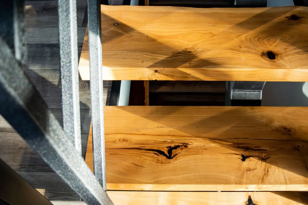 A wooden staircase with three visible steps and black support brackets, next to a dark wooden floor and a metal frame structure.